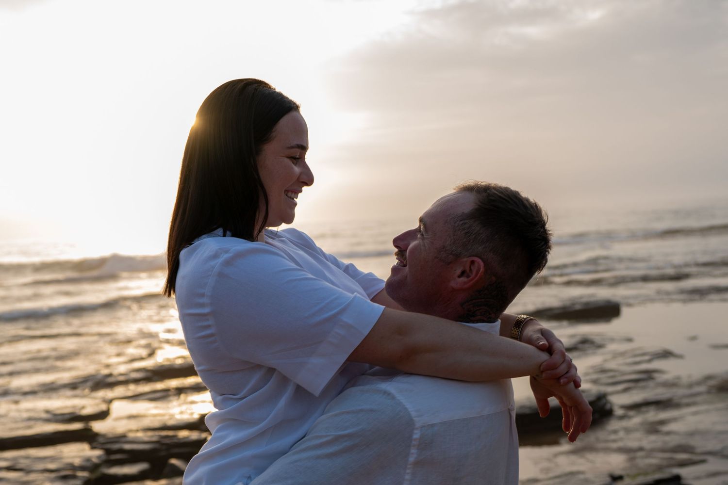 A couple embraces on the beach at sunset creating a romantic silhouette against the golden sky.