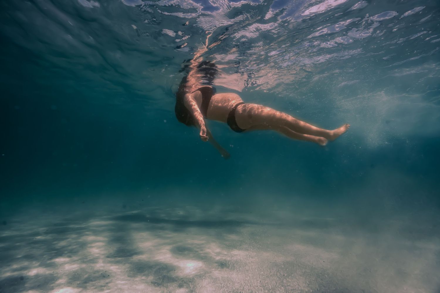 A person swims gracefully underwater in a blue ocean, creating a serene and peaceful underwater scene.