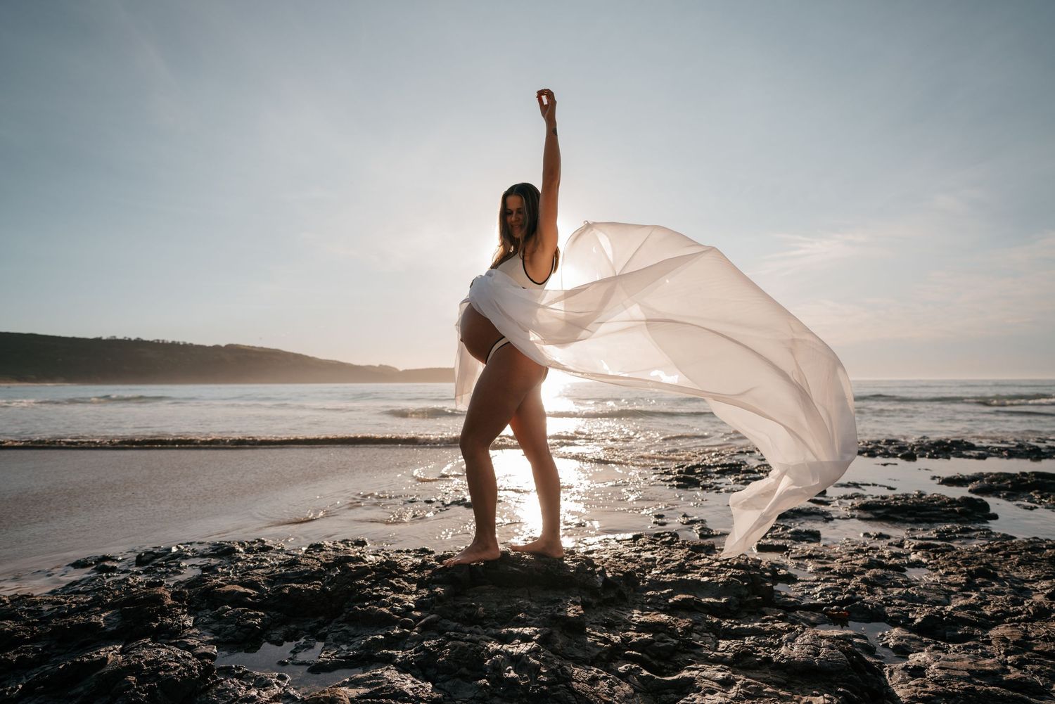 A graceful silhouette on a beach at sunset with flowing white fabric dancing in the wind.