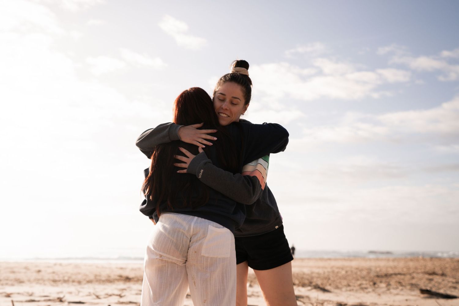 People embracing on beach with soft sunset lighting.