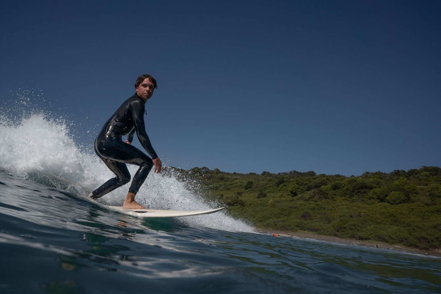 A surfer rides a wave while performing a skilled turn maneuver on a surfboard in blue ocean waters.