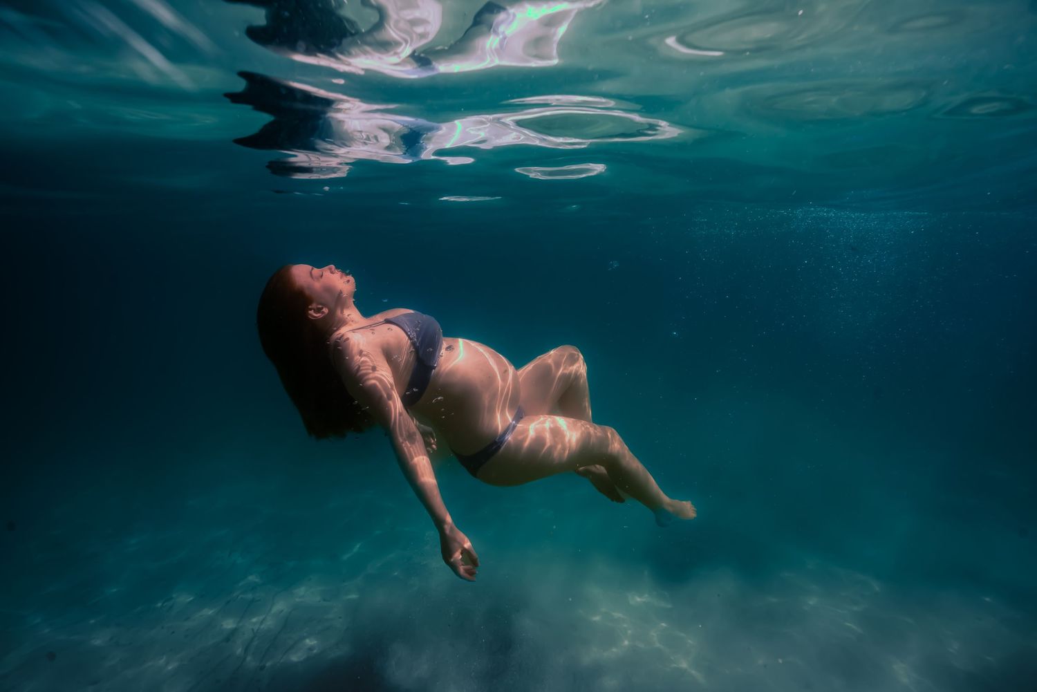 A sequence of underwater photos shows a figure gracefully diving and swimming beneath the turquoise surface.