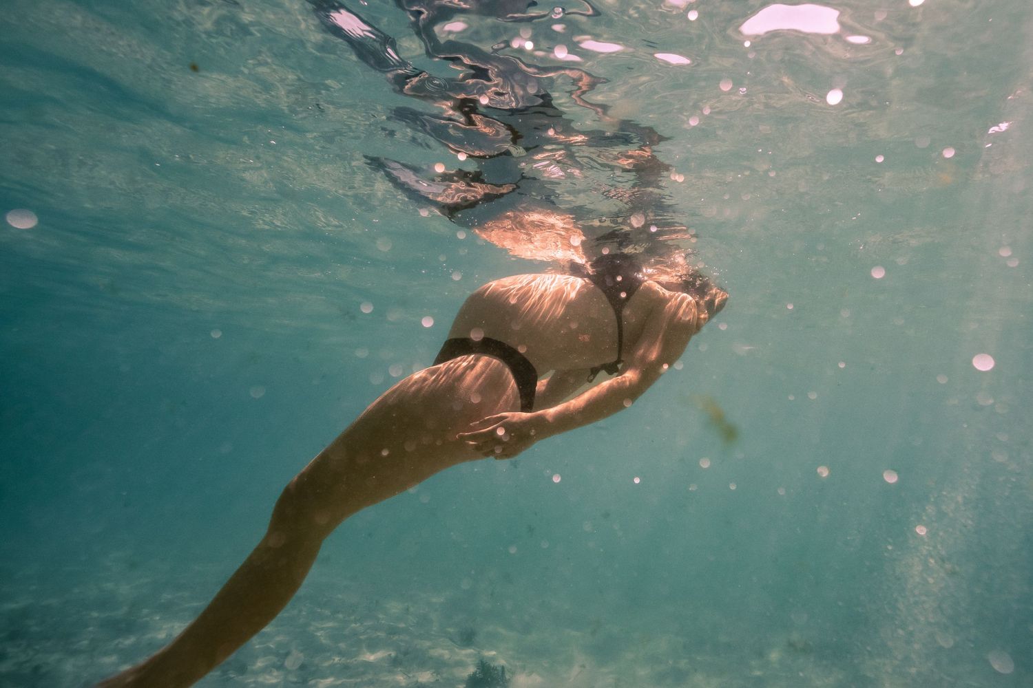 Underwater view of a person swimming gracefully through clear blue water with bubbles trailing behind them.