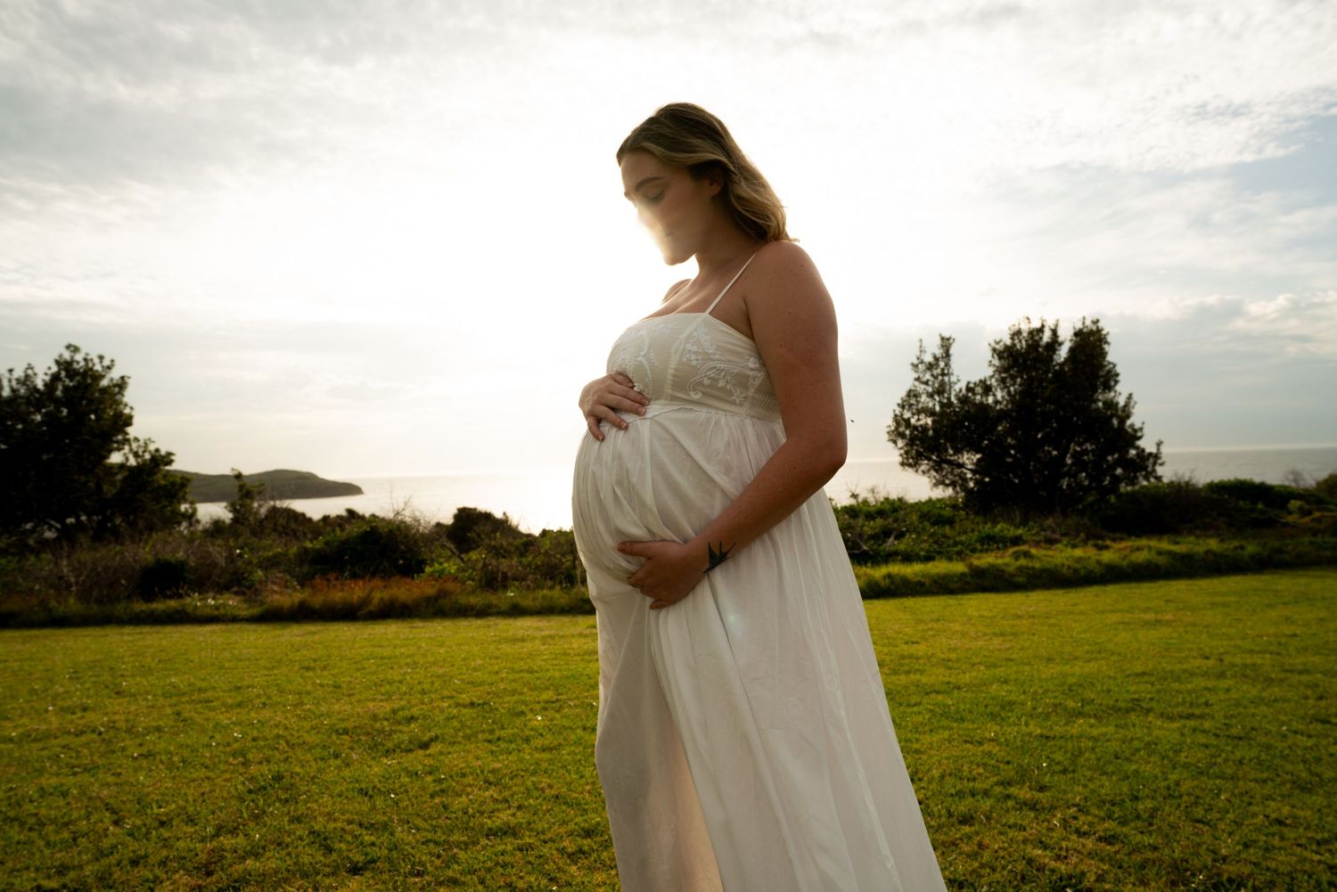Maternity photos in white dress taken in golden sunlit field.