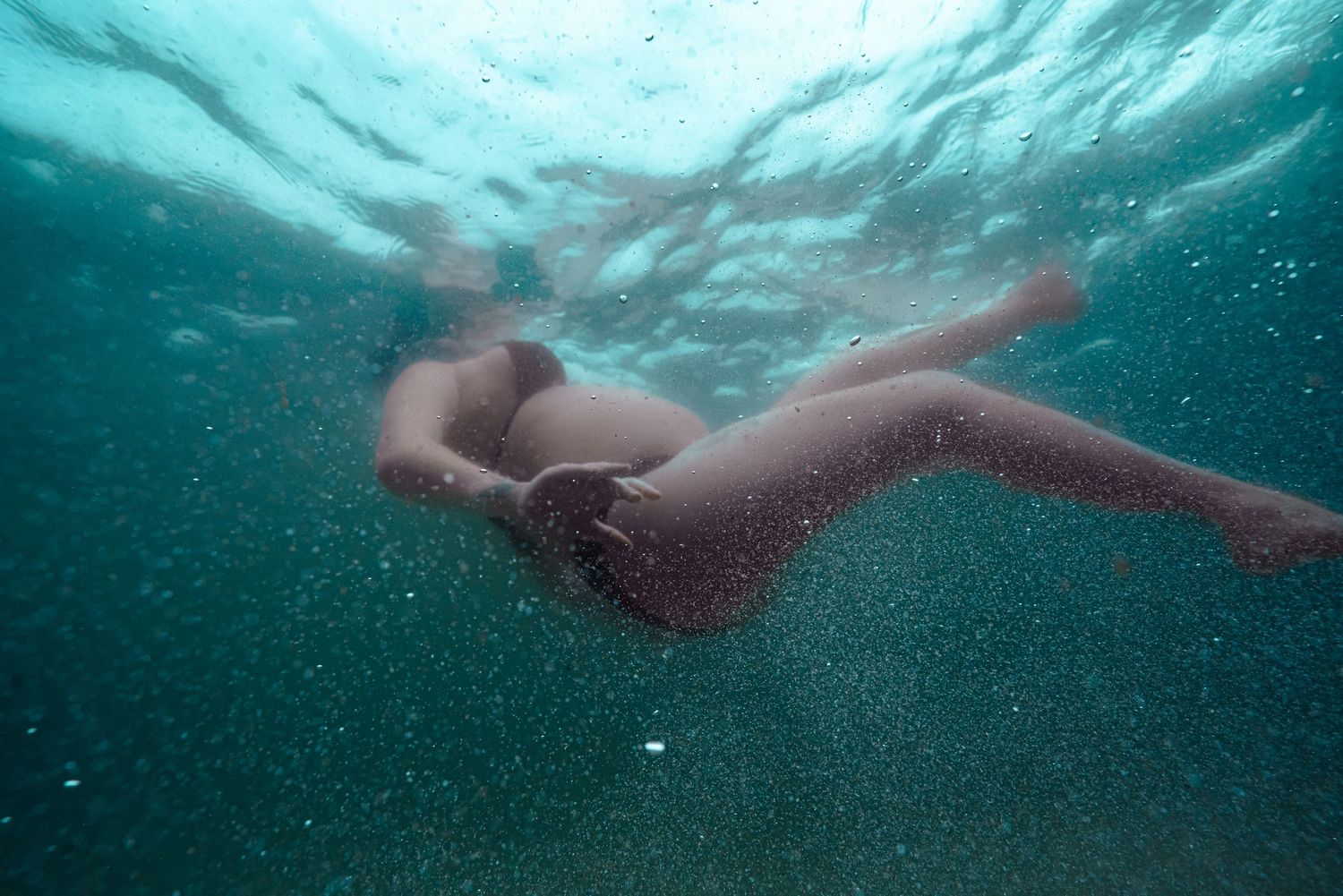 Underwater view of swimmers in a pool with bubbles and rippling water creating a dreamy aquatic scene.