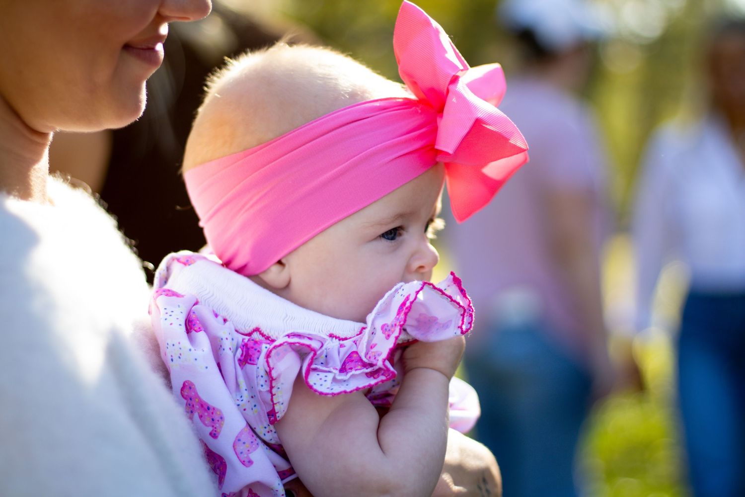 Baby wearing pink accessories at an outdoor event.