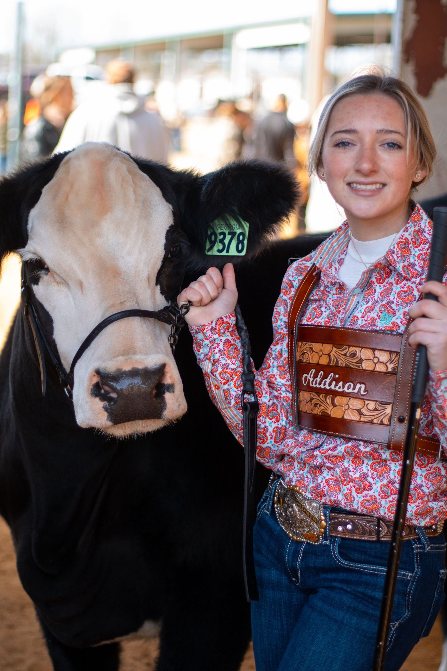 A dairy cow and exhibitor wearing a red patterned shirt pose together at a livestock show.