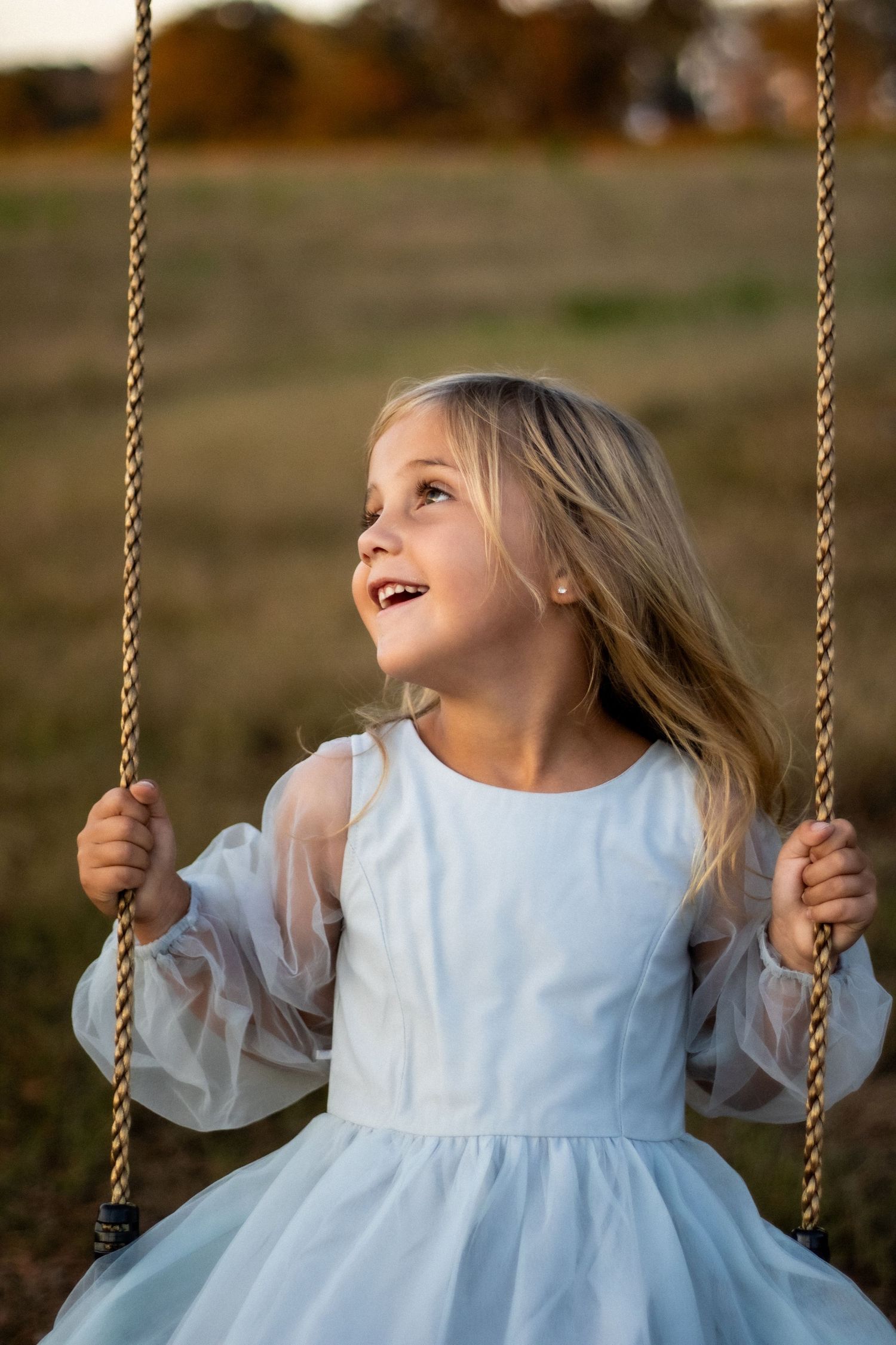 A light blue dress catches the sunlight while on a wooden swing.