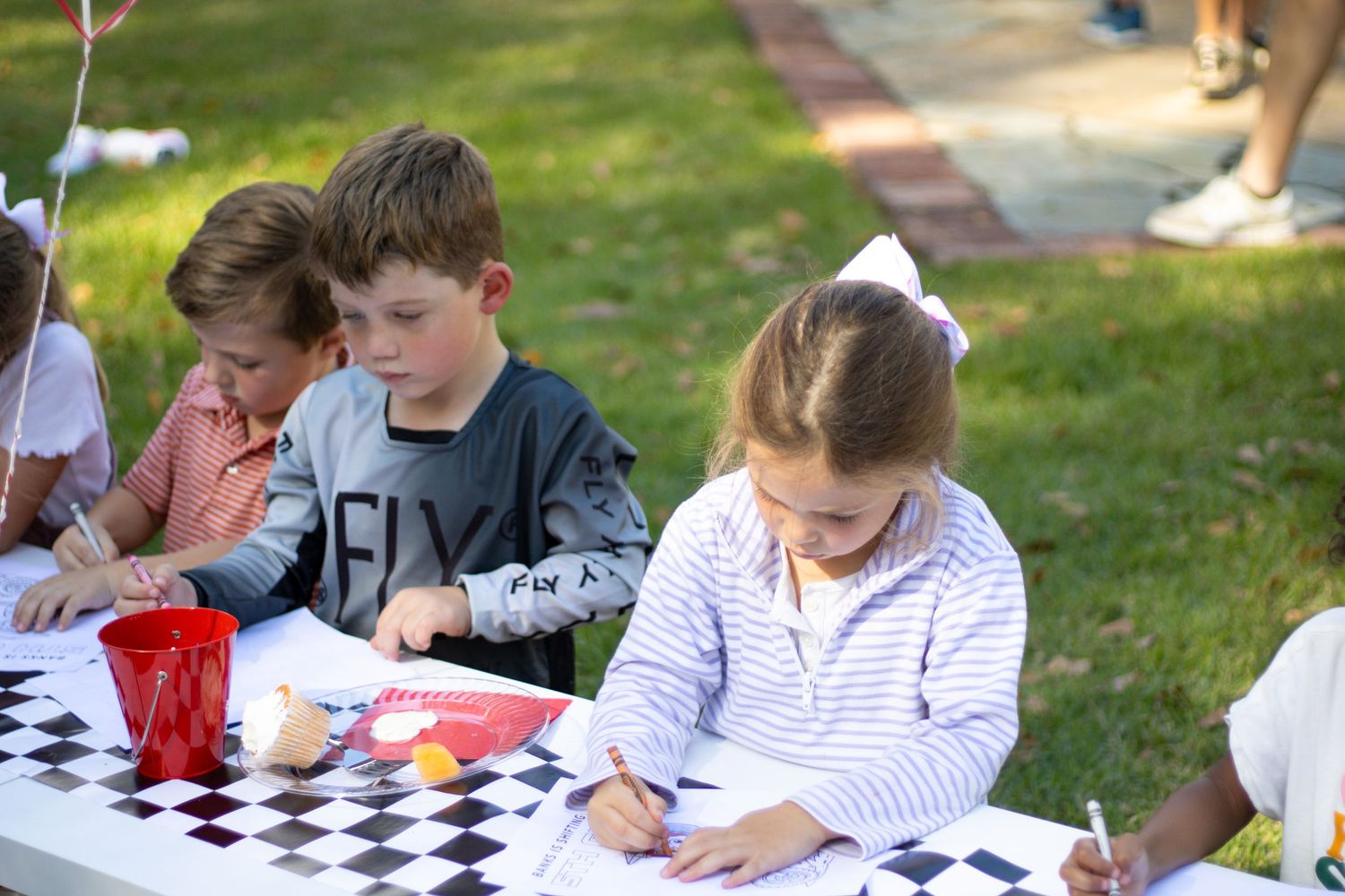 Children sitting at tables doing activities at an outdoor event.