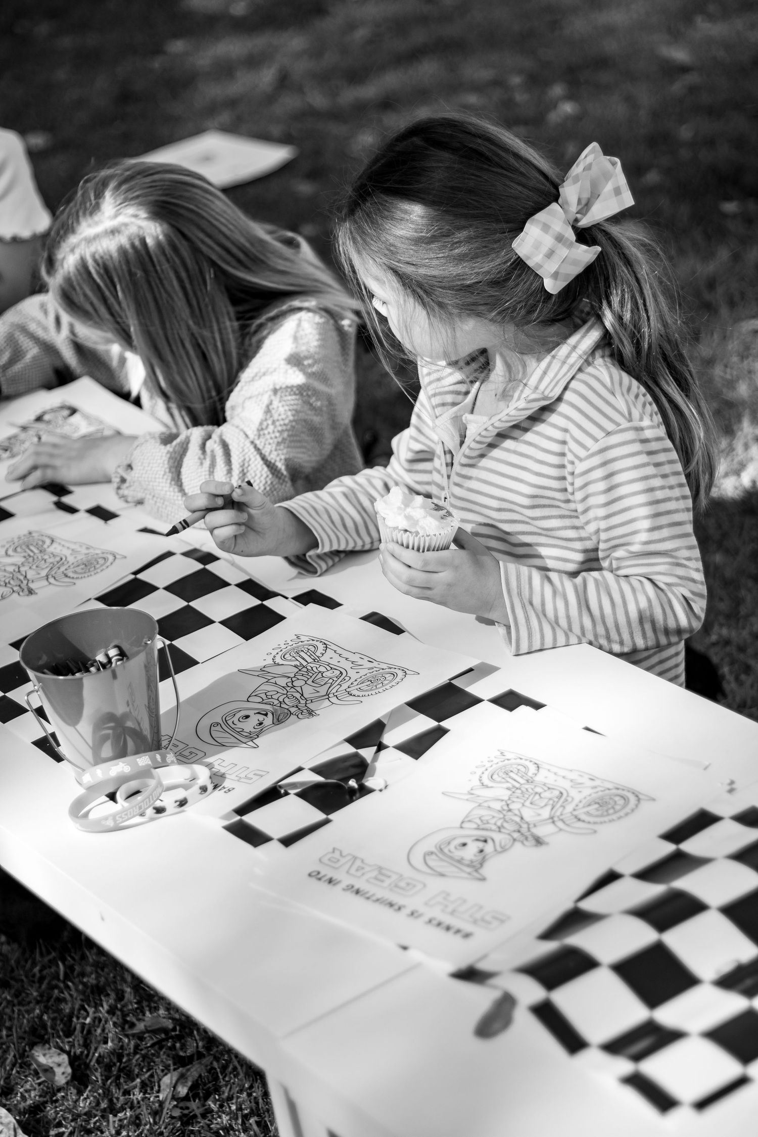 Black and white image of children coloring on checkered paper at a table.