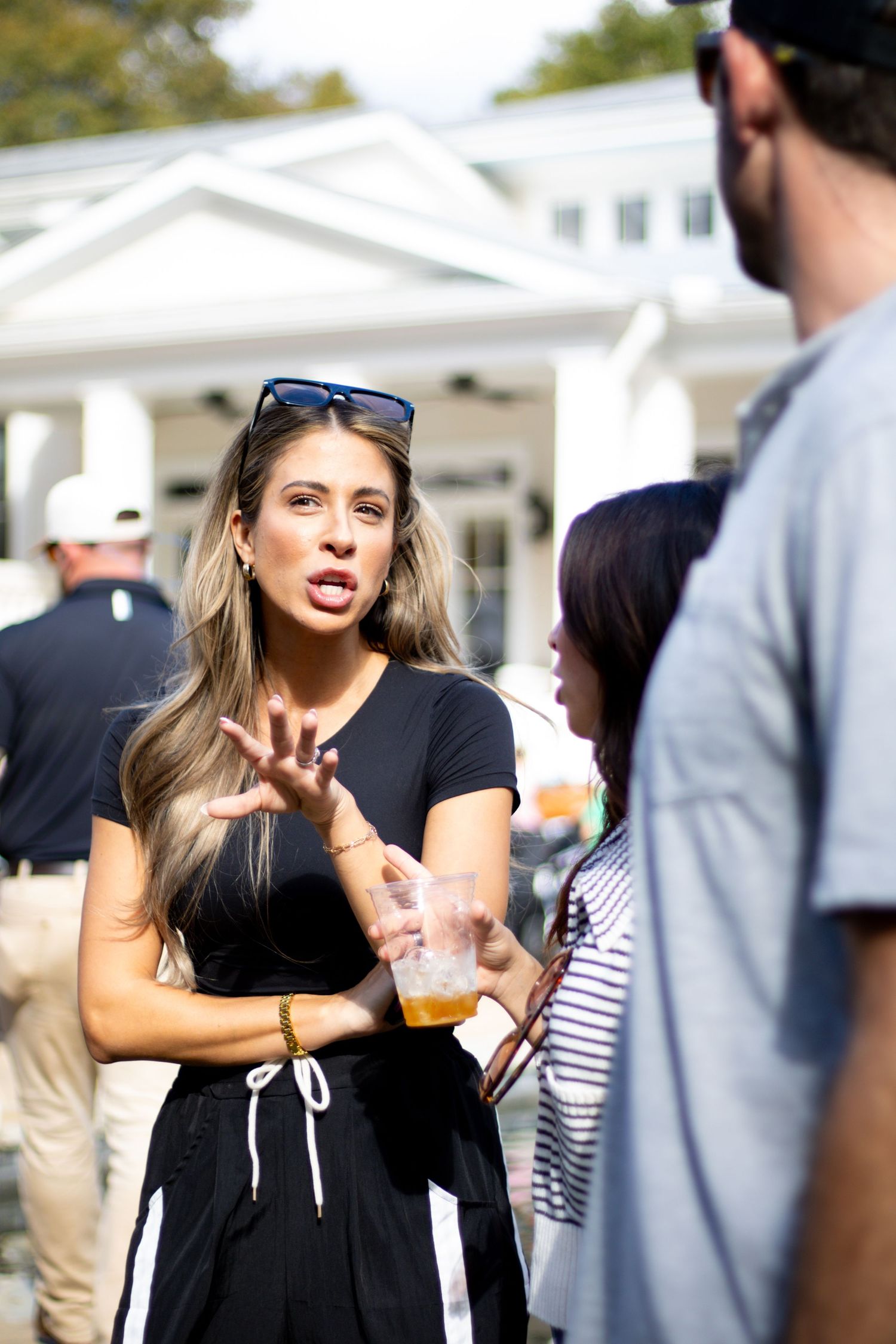 Woman in black dress holding a drink at an outdoor social gathering.