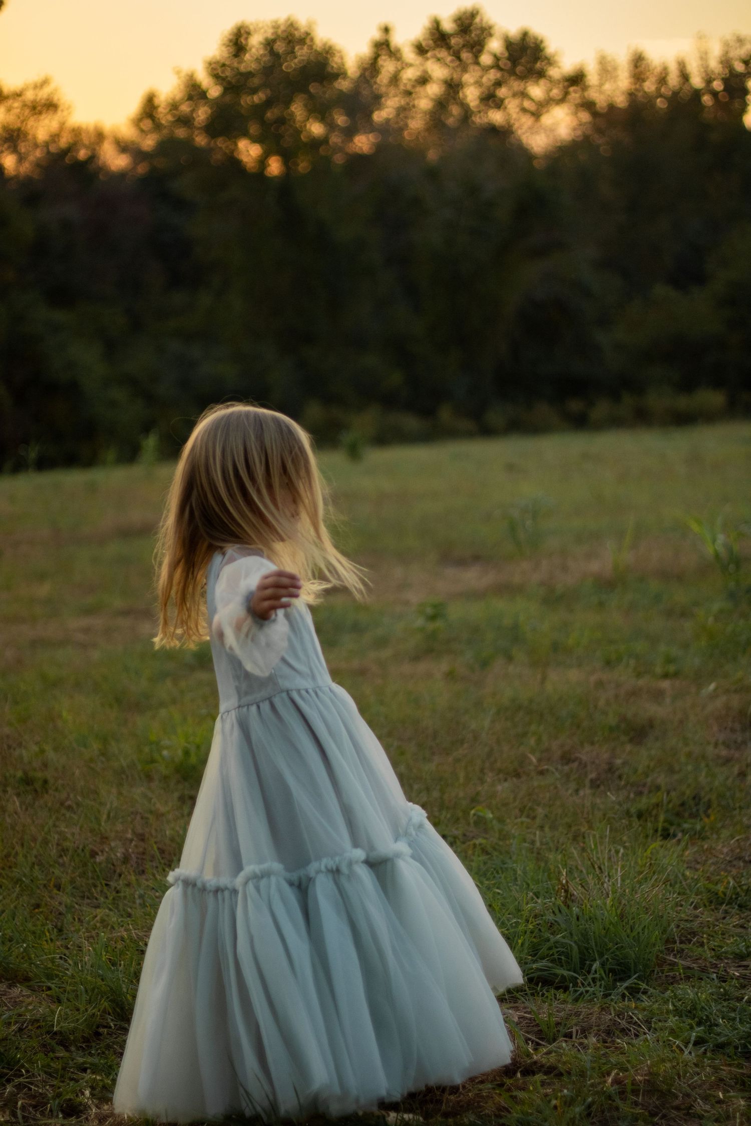 A child twirls in a light blue dress during golden hour in an open field.