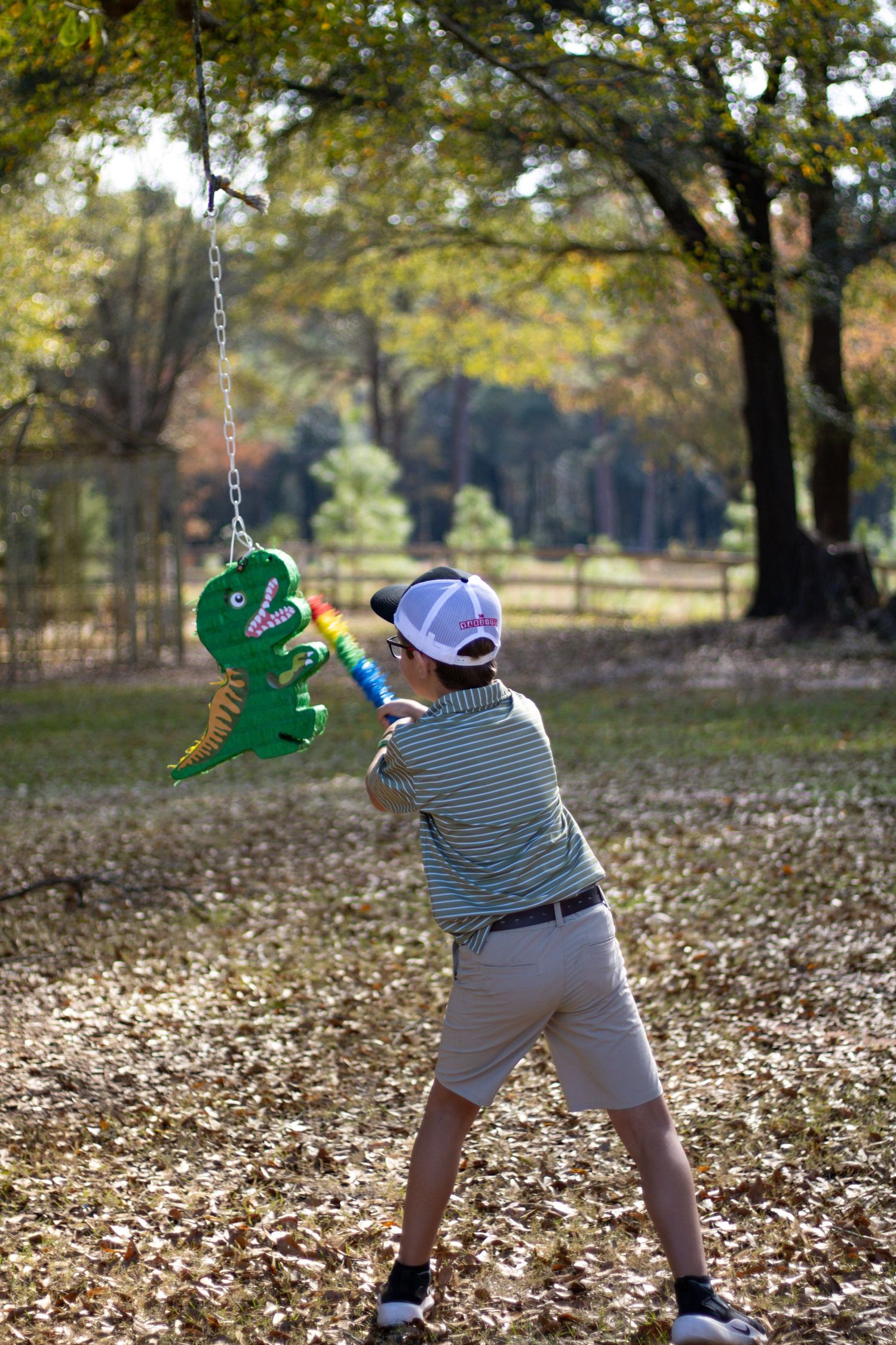 Child playing with a green dinosaur toy in a park filled with autumn leaves.