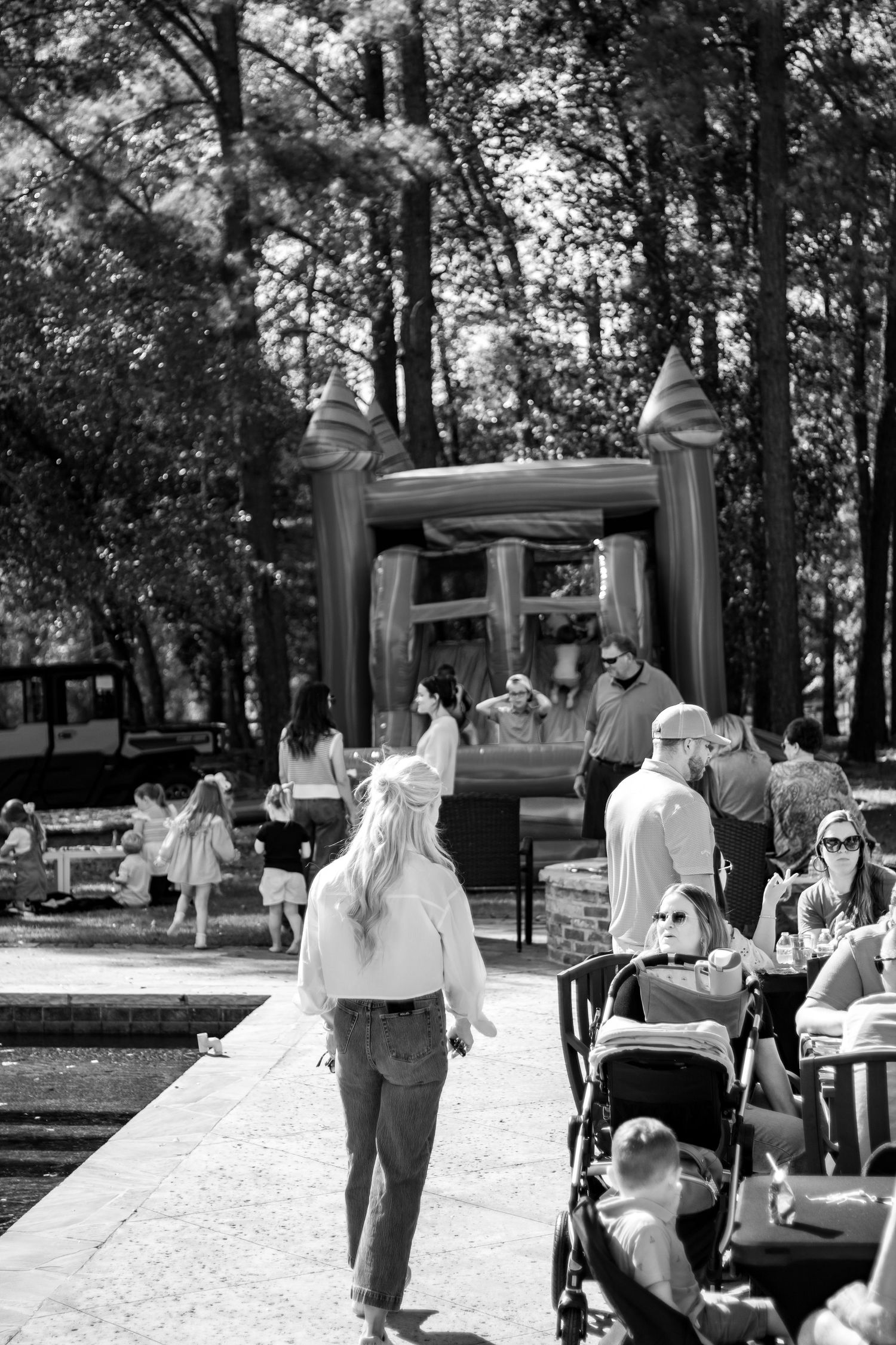 People gather outdoors at a casual event with cars and trees in the background.