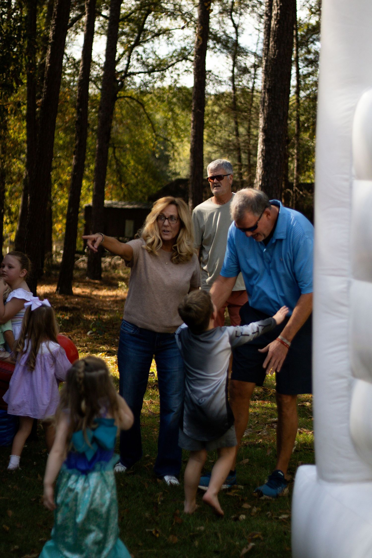 A group plays an outdoor game involving white inflatable objects in a wooded area.