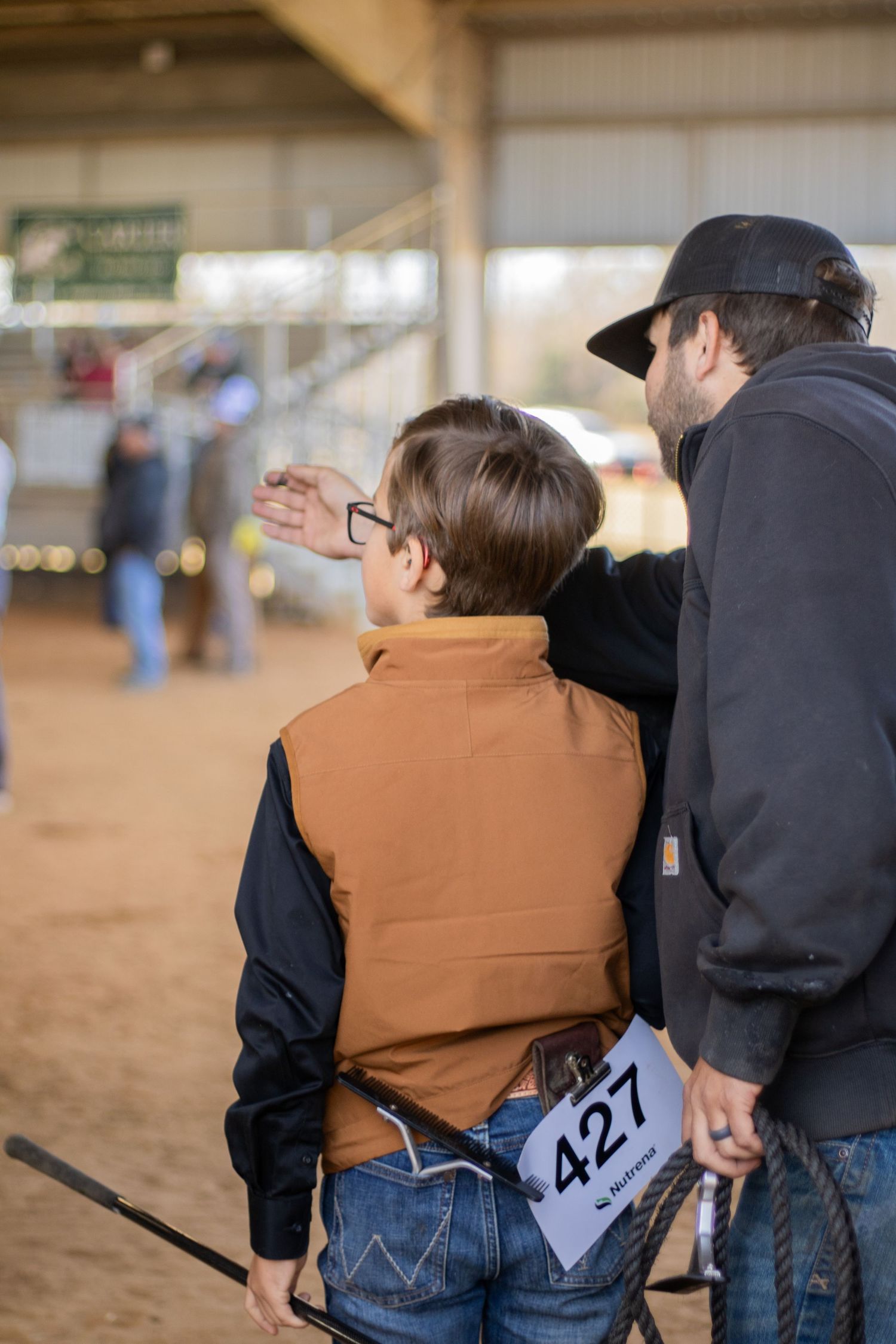 Three people in jeans and western wear stand together at what appears to be a rodeo or equestrian event.