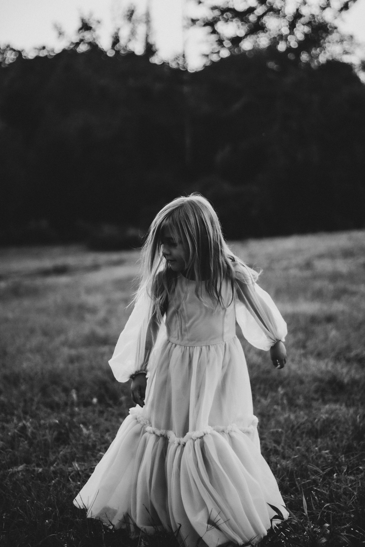A series of black and white images showing a person in a white flowing dress sitting in a grassy field at dusk.