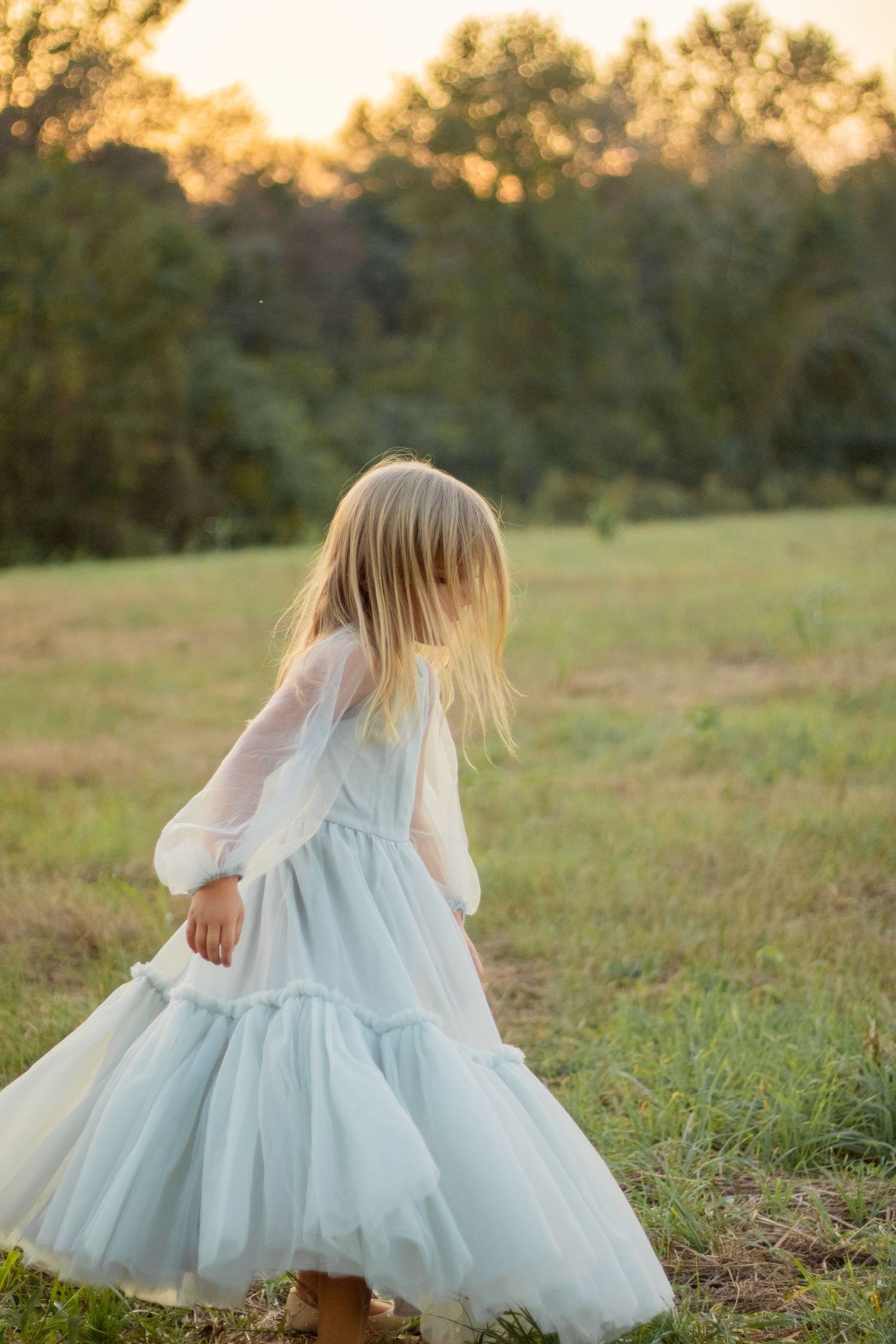 A flowing light blue dress twirls in a golden sunset field.