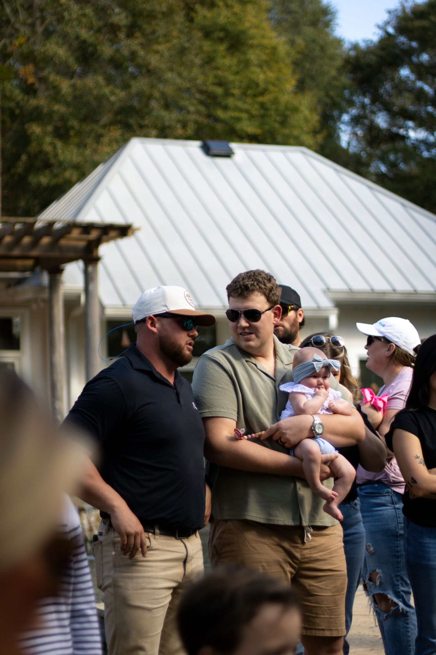 Group of people gathered outdoors in front of white buildings during a social event.