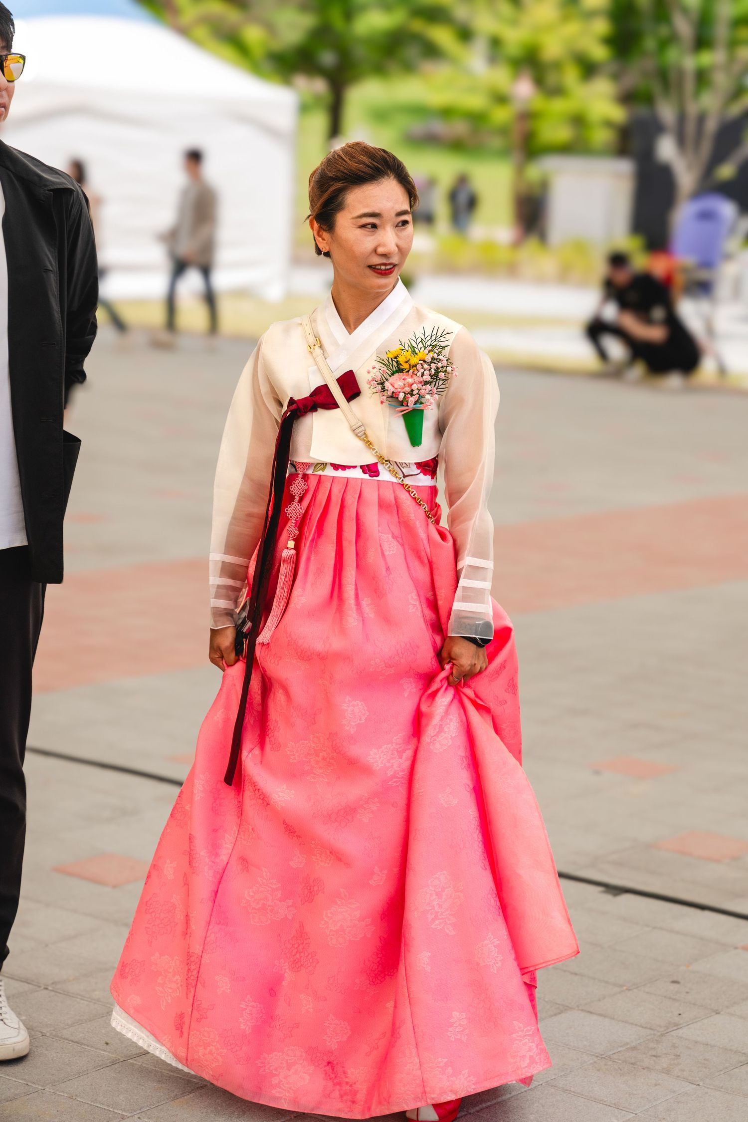 A person wearing a traditional pink and white hanbok dress walks outdoors in a public space.