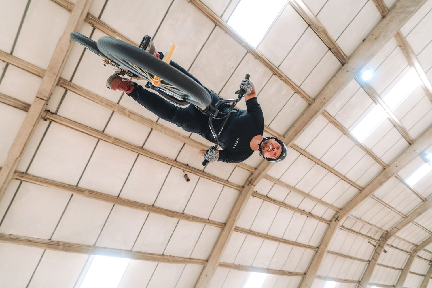 BMX rider performing an upside-down aerial trick inside a warehouse, captured from below showing impressive bike control.