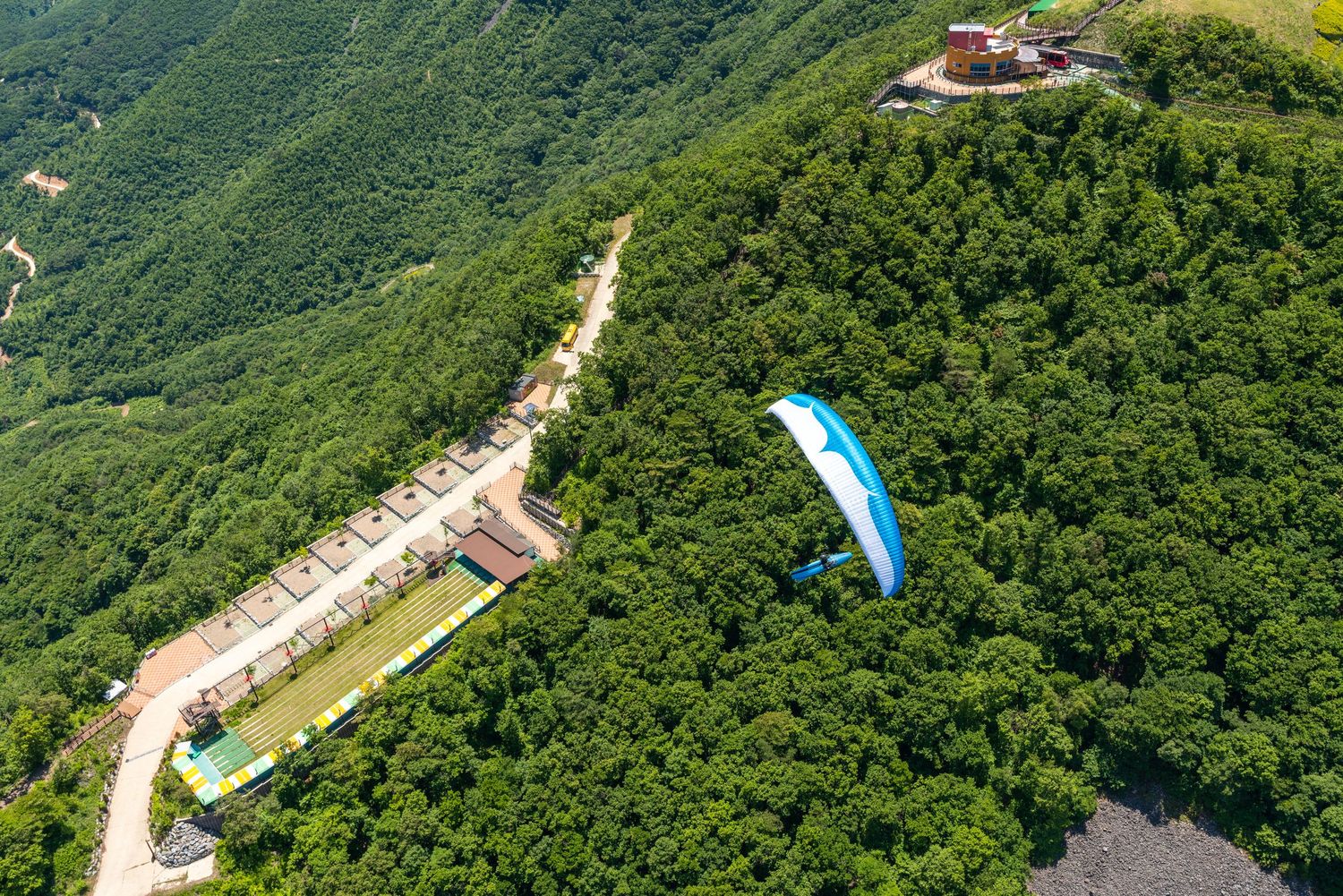 Aerial view of paragliders soaring over lush green mountain terrain with winding roads below.