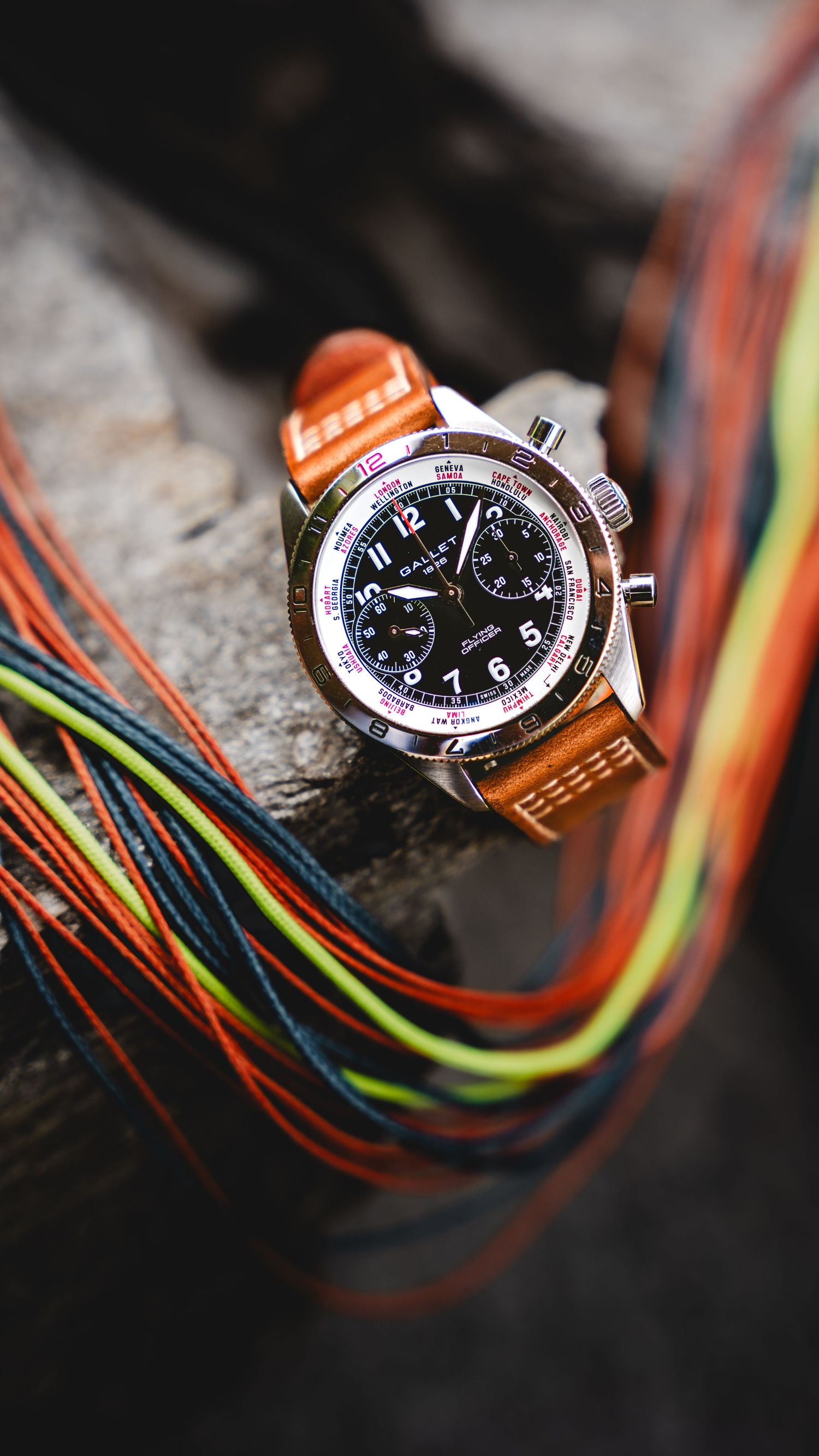 A luxury chronograph watch with brown leather strap resting on colorful braided ropes outdoors.