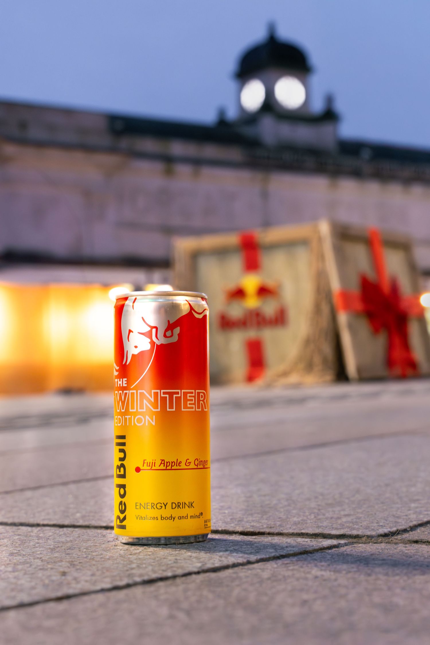 A row of yellow Red Bull energy drink cans lined up on a concrete surface at dusk with warm lighting.