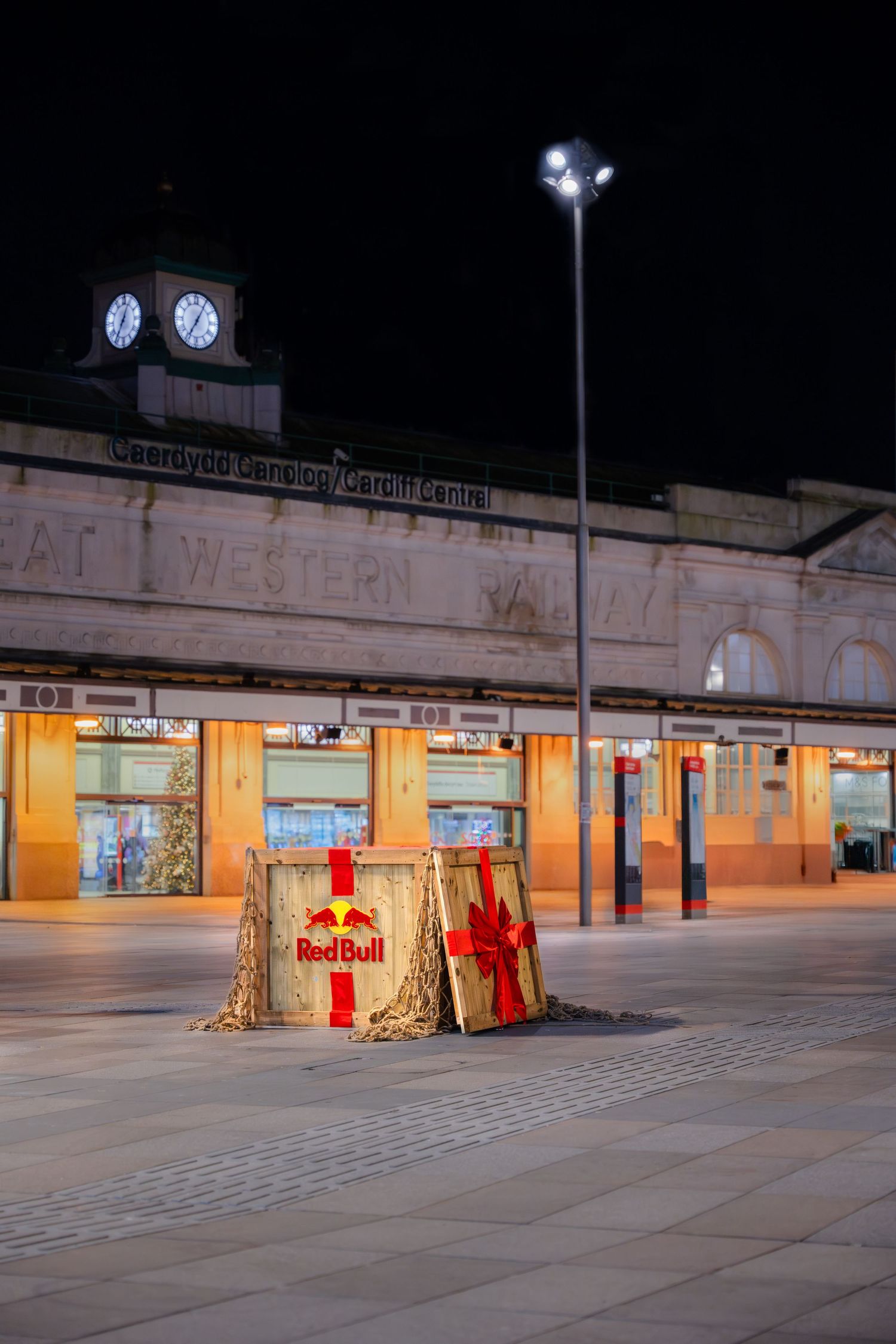 Red Bull branded structure outside Cardiff Central station at night, with clock tower and Great Western facade illuminated.
