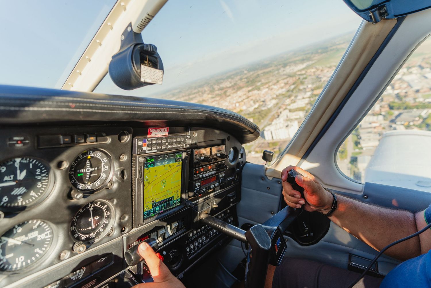 View from inside aircraft cockpit showing instrument panel and controls during flight over coastal landscape.
