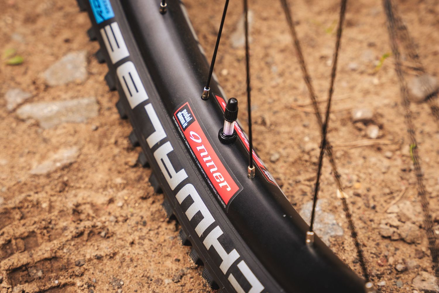 Close-up view of a black mountain bike tire with Maxxis branding on dirt trail surface.