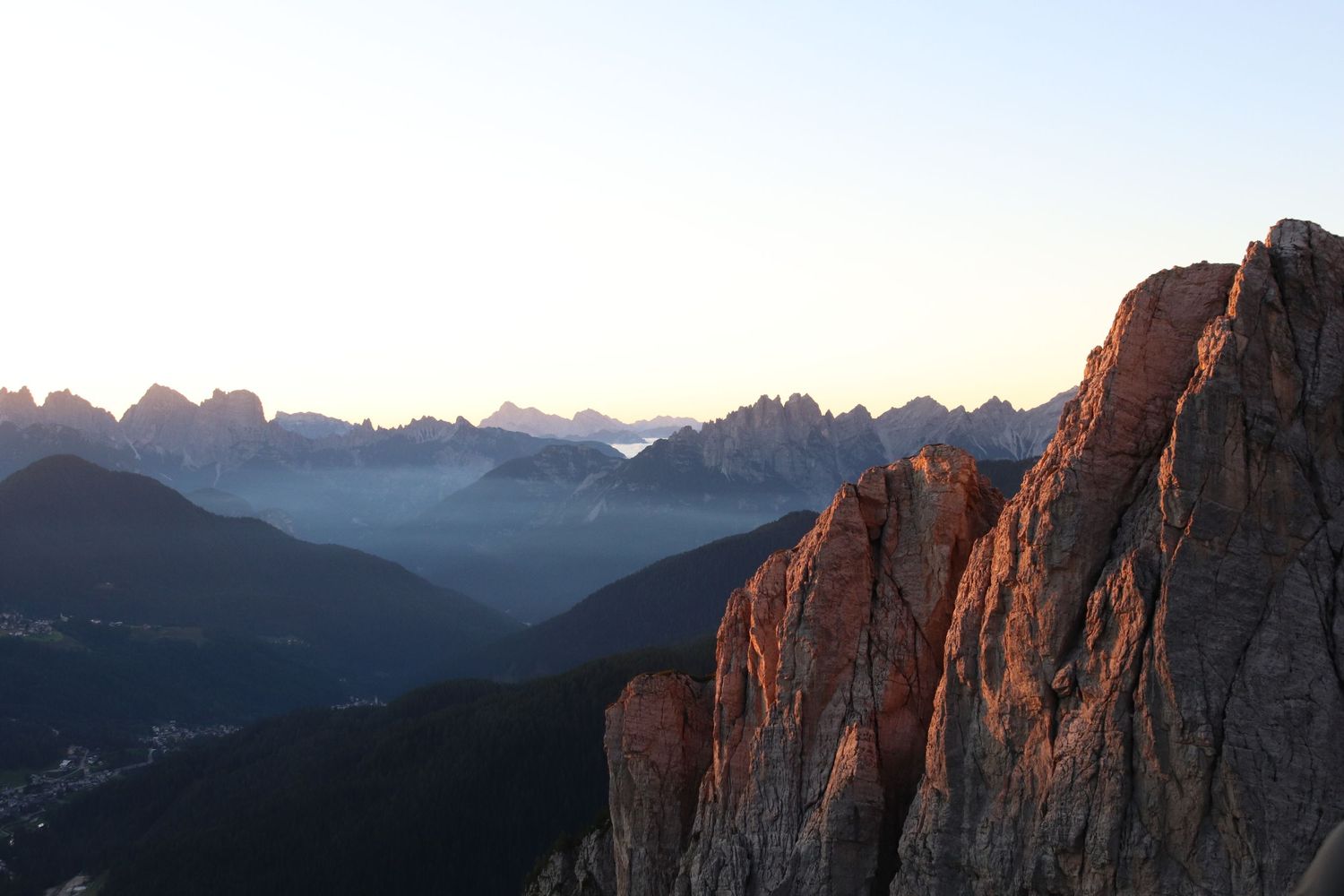 Dramatic mountain cliffs bathed in golden sunset light with layered peaks silhouetted against a fading sky.