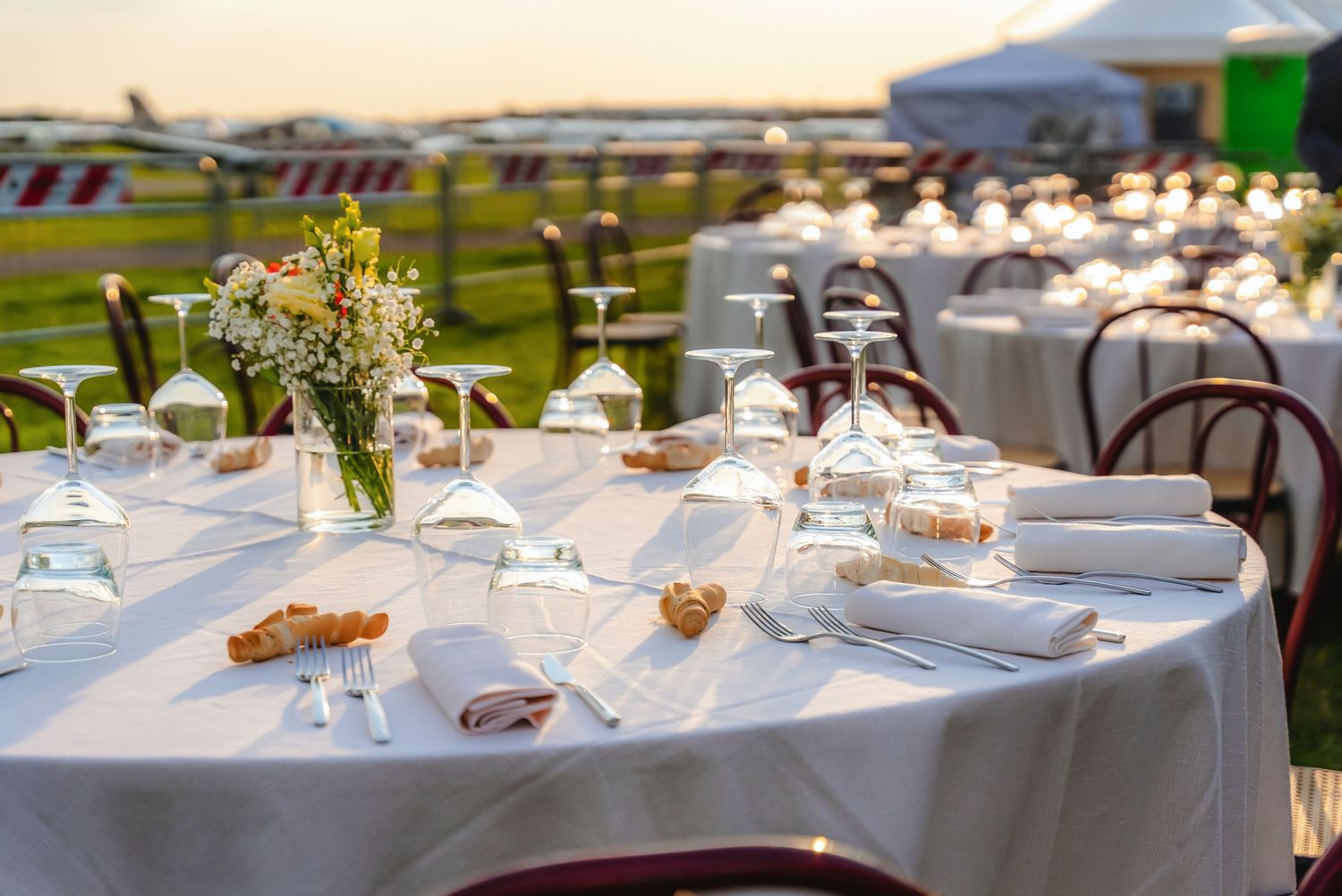 Elegant outdoor wedding reception tables set with white linens, floral centerpieces and place settings under a tent canopy.