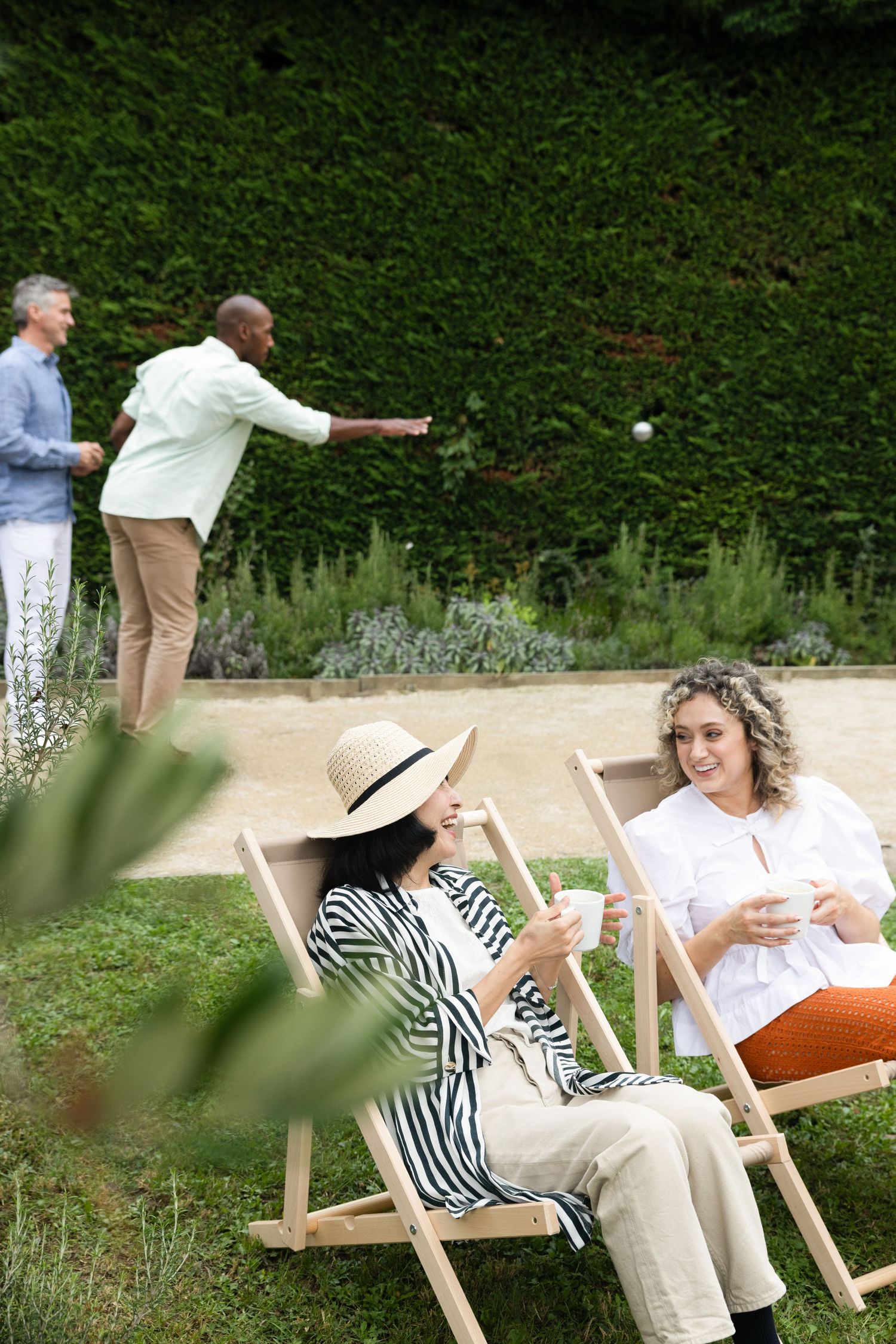 People enjoying a game of lawn bowling in a garden setting with white chairs and lush greenery in the background.