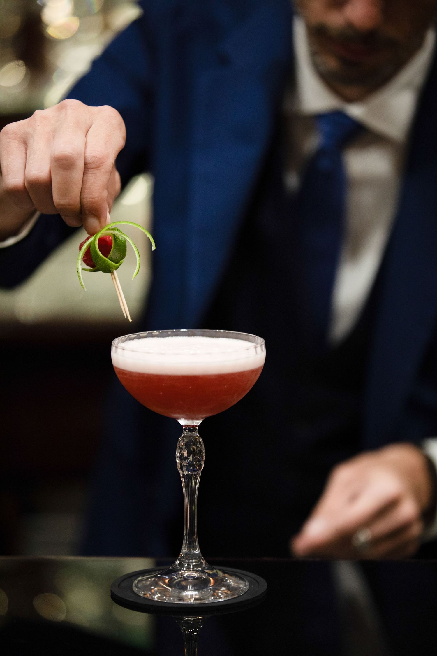A bartender garnishes a pink cocktail in a coupe glass with a delicate lemon twist.