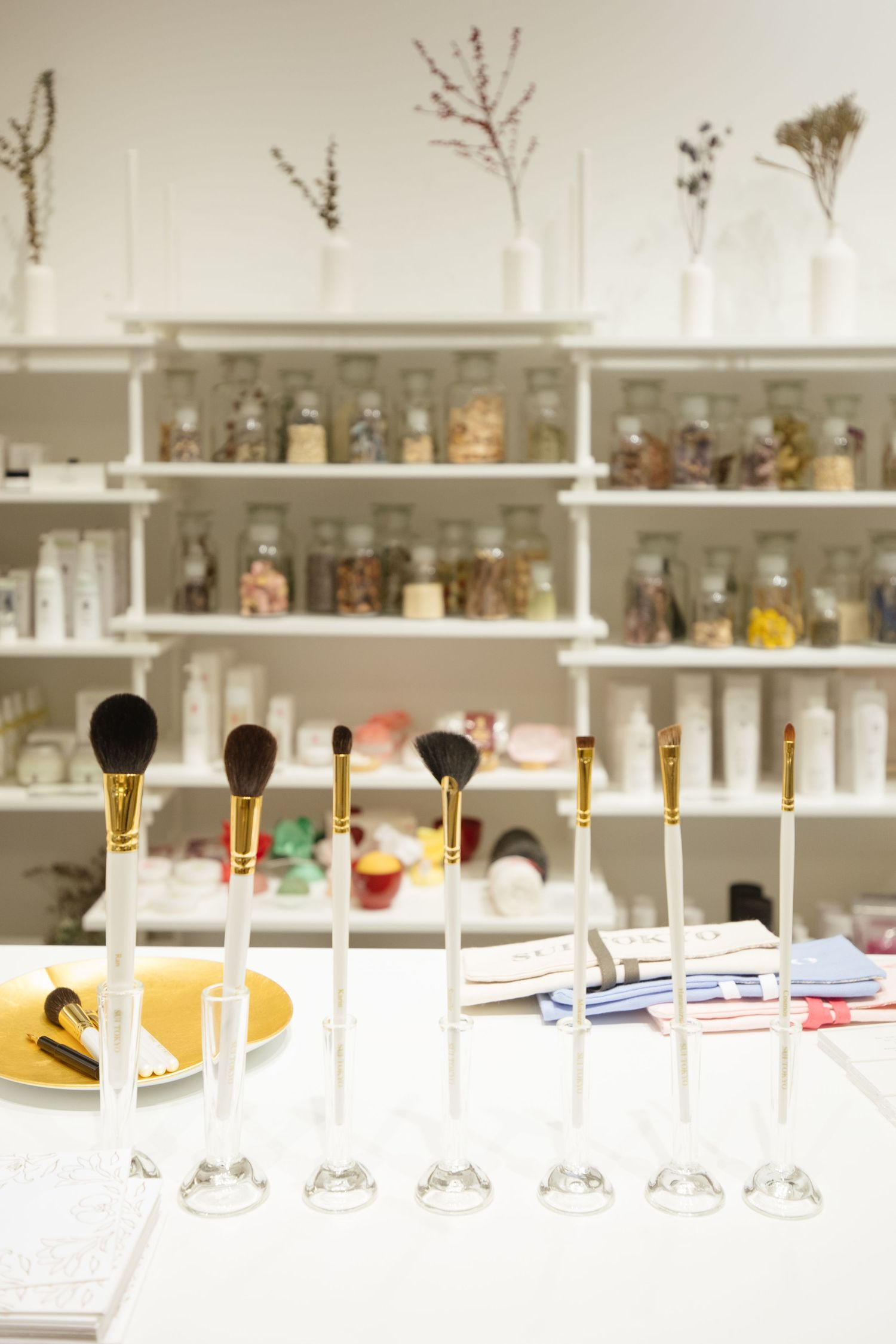 Row of elegant cocktail glasses lined up on a white bar counter with various bottles and glassware displayed on shelves behind.