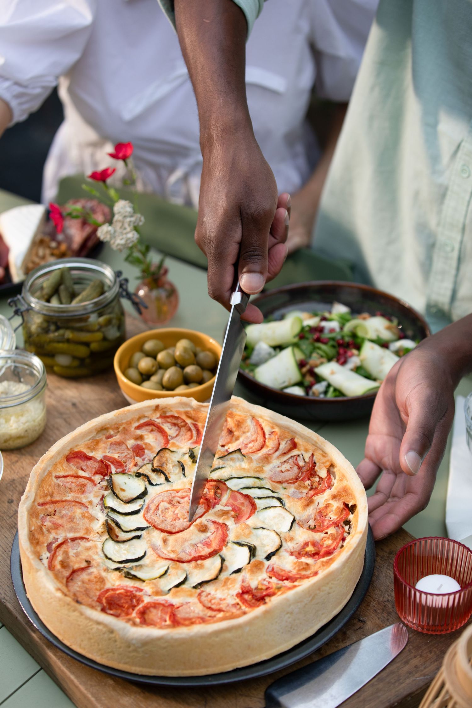 A sequence of pizza preparation steps showing hands arranging toppings on a round pizza with olives and vegetables.