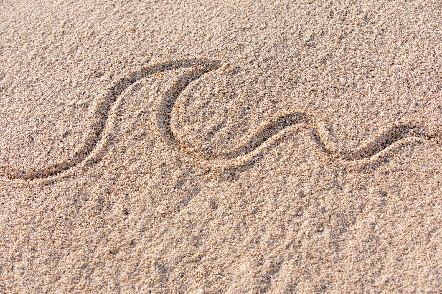A close-up view of a sandy beach surface with rippled patterns and textures in natural beige tones.