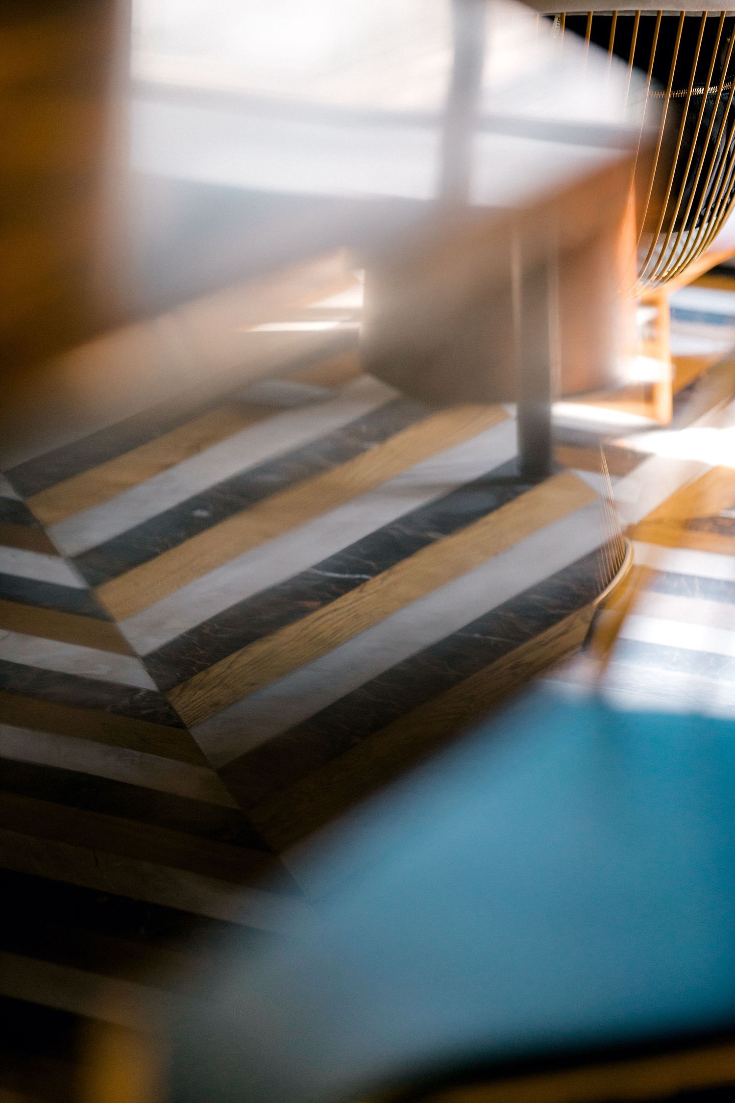 Abstract geometric pattern with diagonal stripes in gold and gray tones viewed through a blurred foreground element.