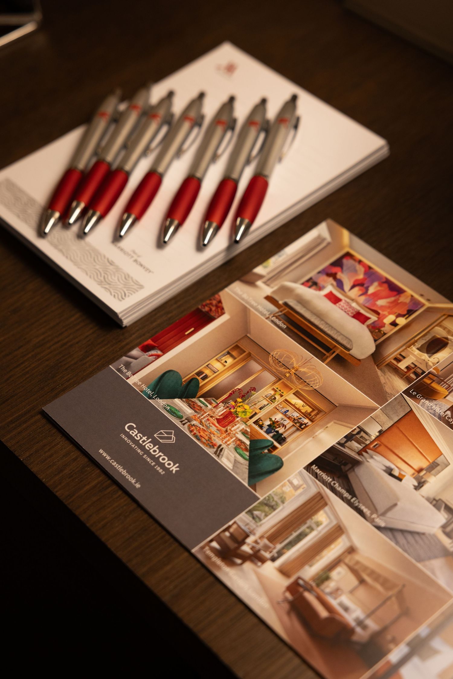 A series of printed marketing brochures or catalogs arranged in a row on a dark wooden surface showing interior design layouts.