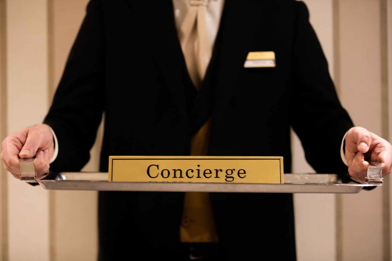 Hotel concierge staff member stands behind desk wearing black uniform while assisting guests with service.