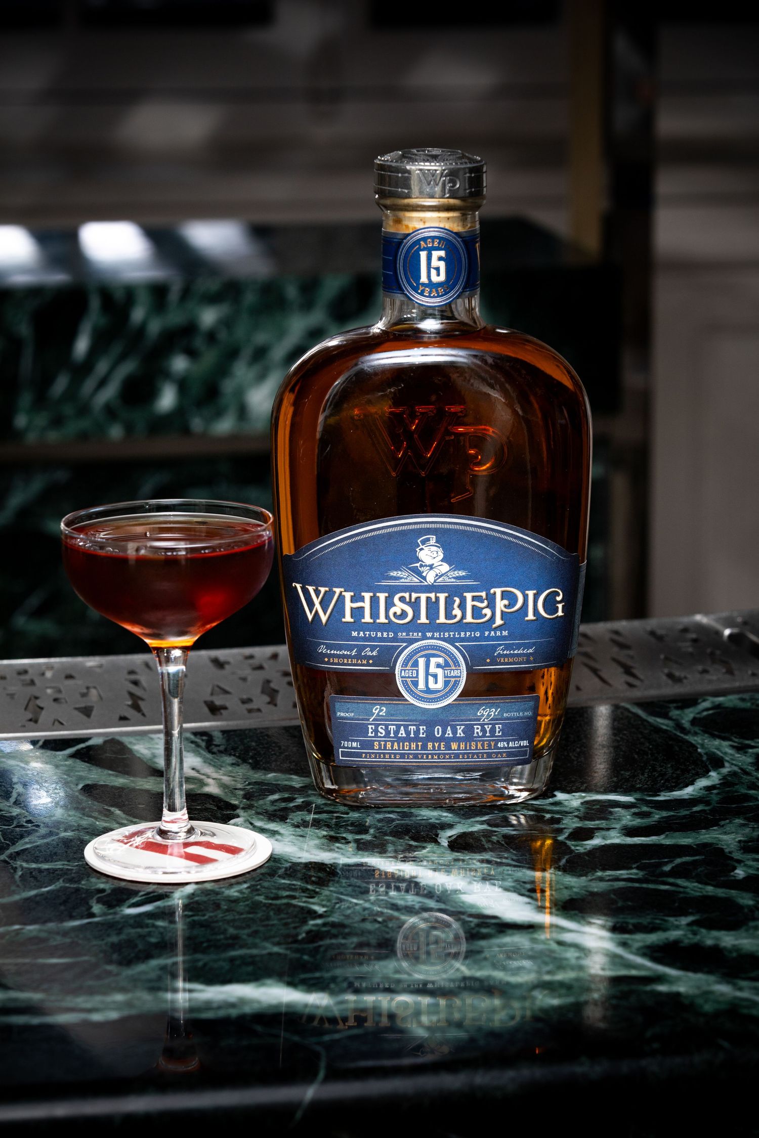 A bottle of WhistlePig 15 year old whiskey and cocktail glass on dark marble surface with dramatic lighting.