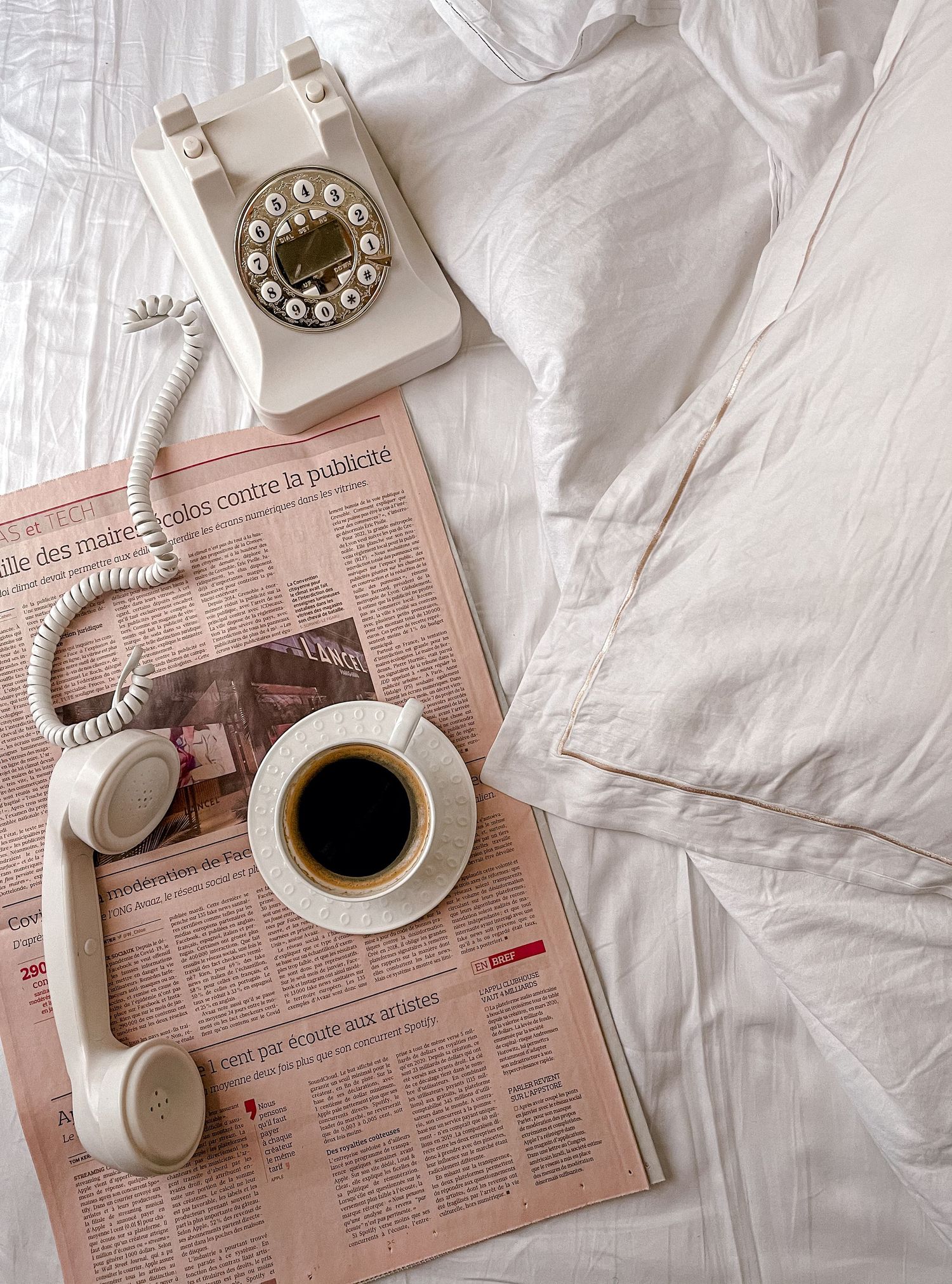 A series of minimalist photos showing a white coffee cup and newspaper on crumpled white bedsheets in morning light.
