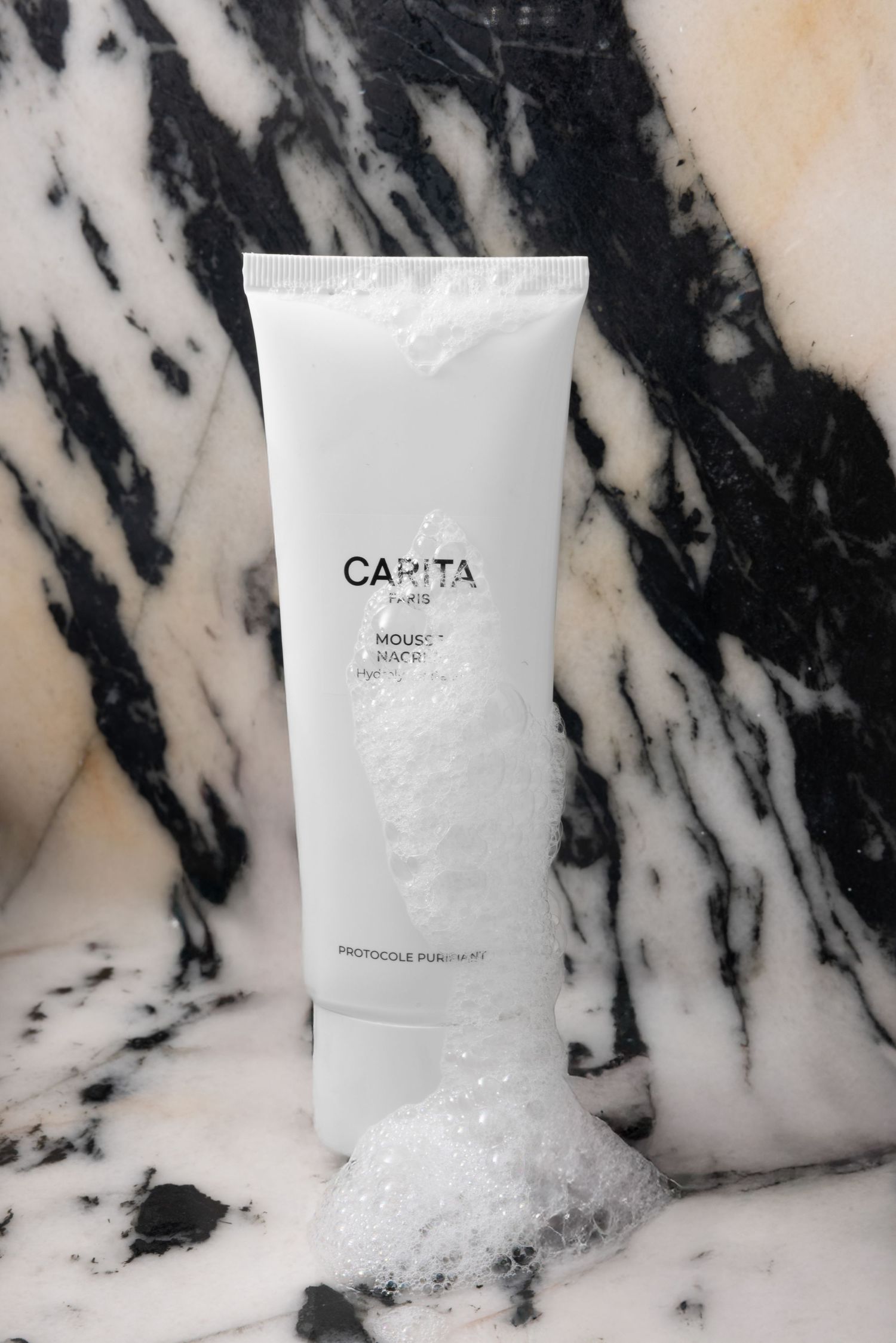 White skincare product bottle displayed on luxurious black and white marble surface with dramatic veining pattern.