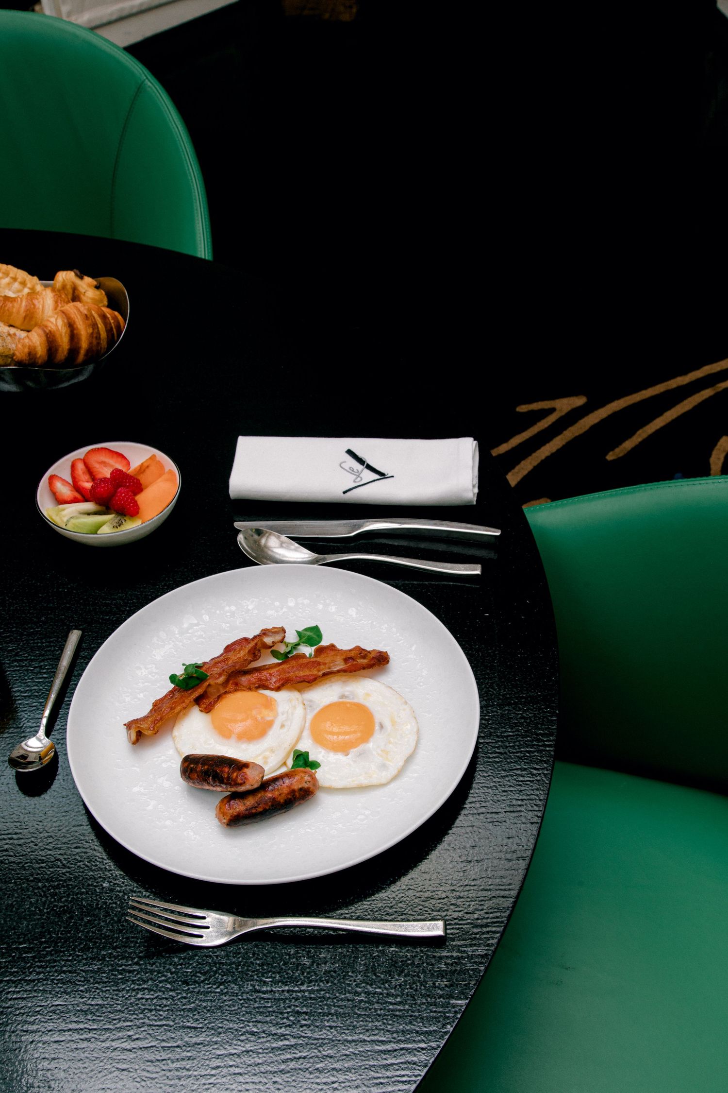 A breakfast plate with sunny side up eggs and bacon served on a white plate with green booth seating visible.
