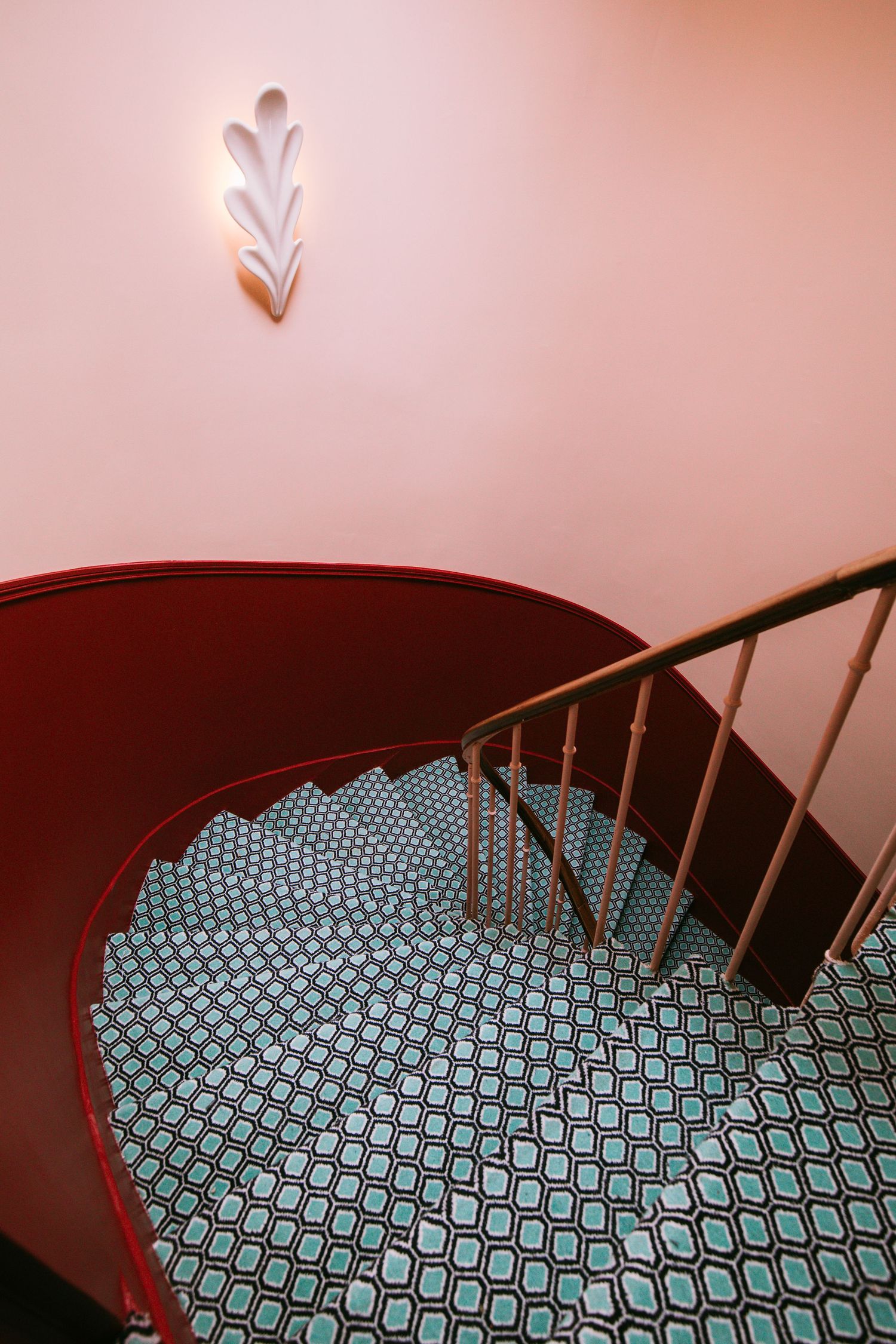 Spiral staircase covered in turquoise and white geometric patterned carpet descending downward in a curved motion.