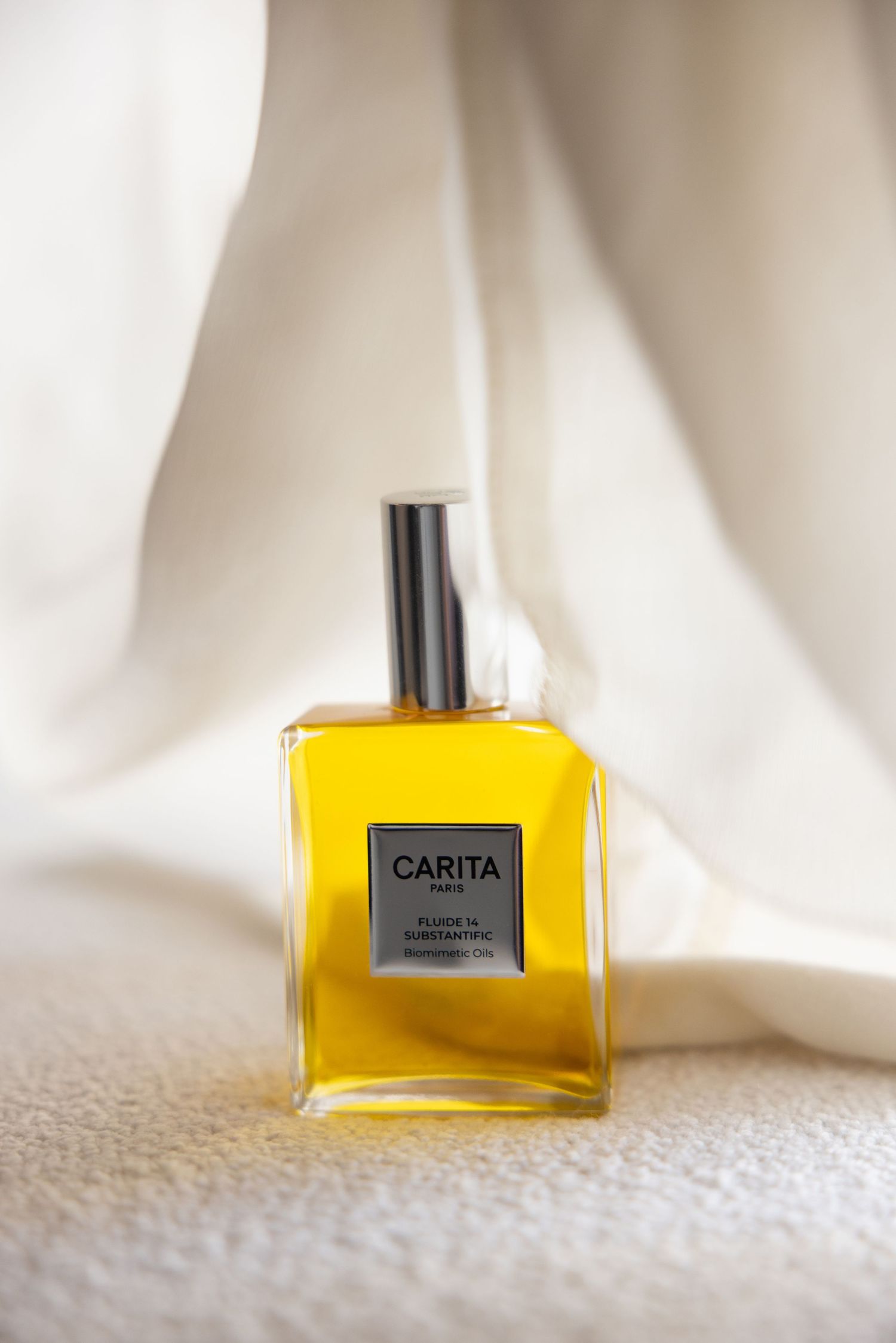 Four identical yellow glass perfume bottles labeled Carita sit on white fabric in a progressive composition.