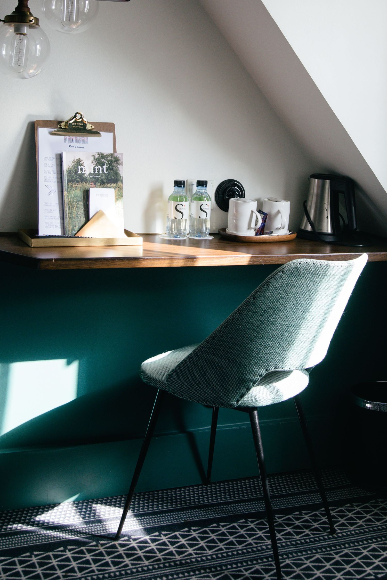 Modern workspace with green walls, white chairs, and wooden shelf under sloped ceiling in attic room.