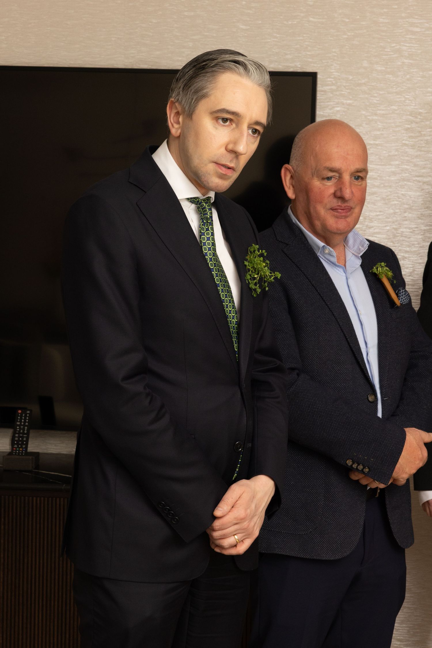 Two men in business attire stand together at a formal event, one wearing a dark suit with green tie and the other in blue.