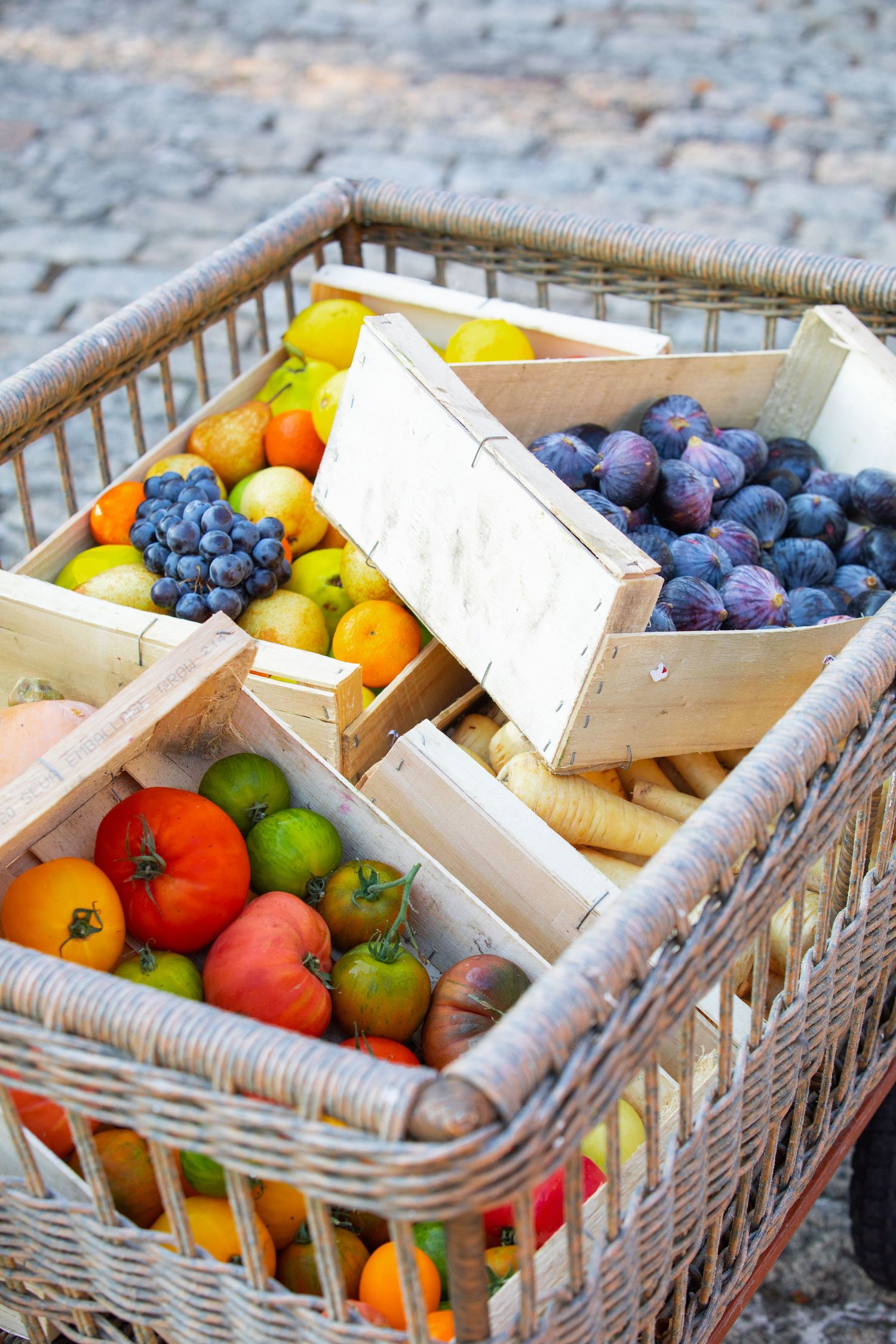 Fresh organic produce including colorful tomatoes and plums displayed in rustic wooden crates and wicker baskets at market.